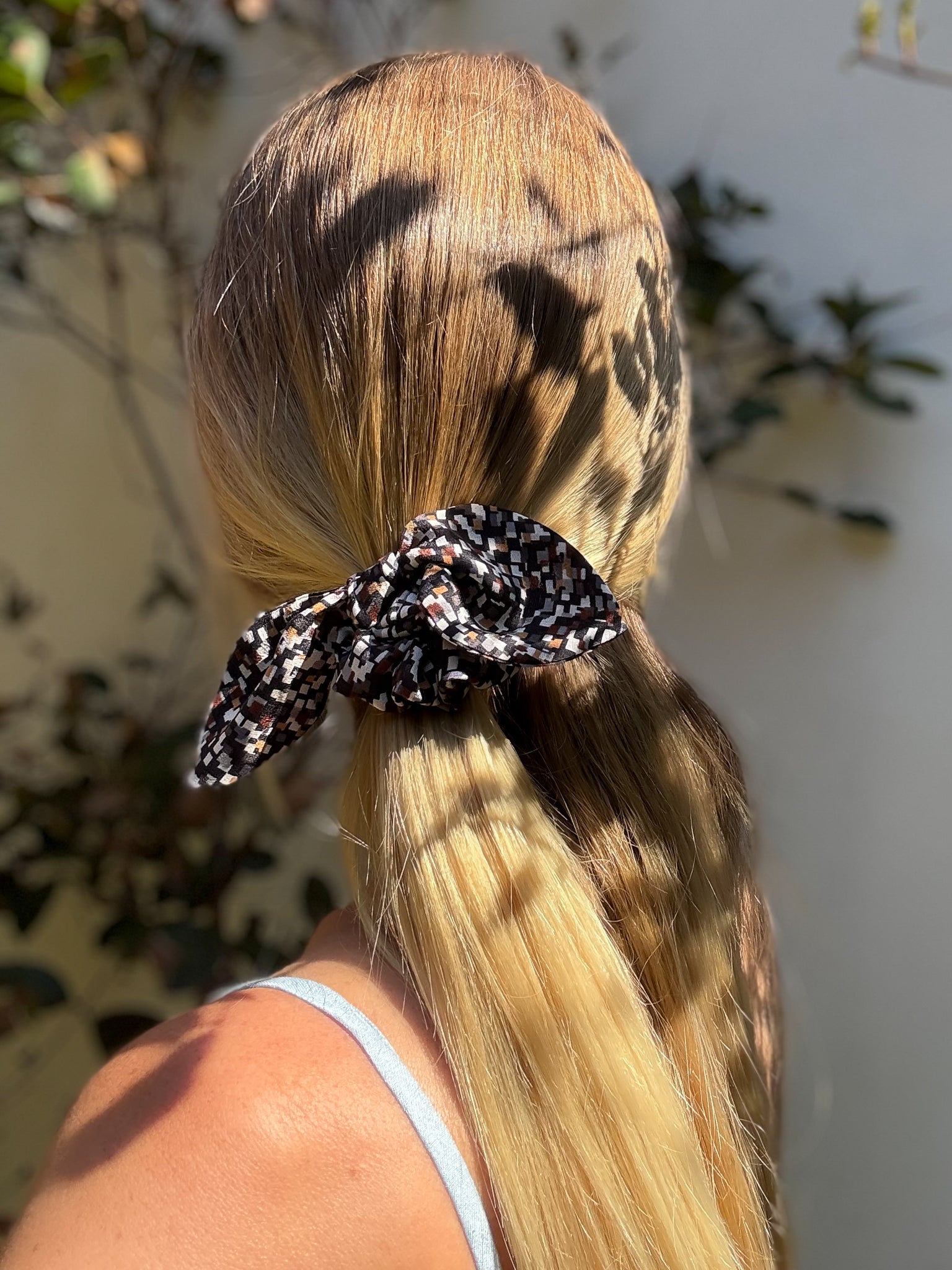 Person with blonde hair tied back with a patterned silk scrunchie, outdoor setting