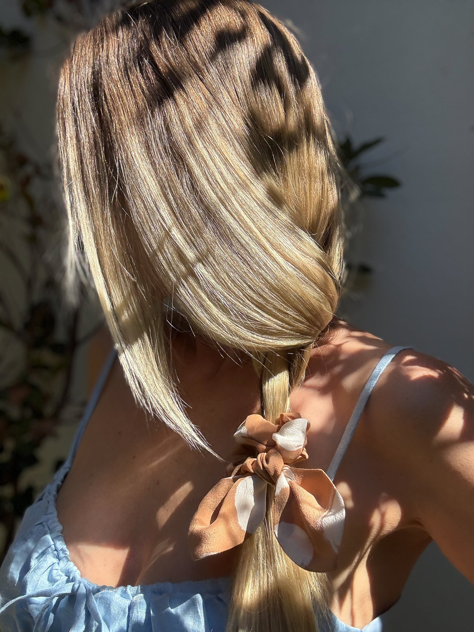 Person with long blonde hair tied back with a brown scrunchie, wearing a light blue top.