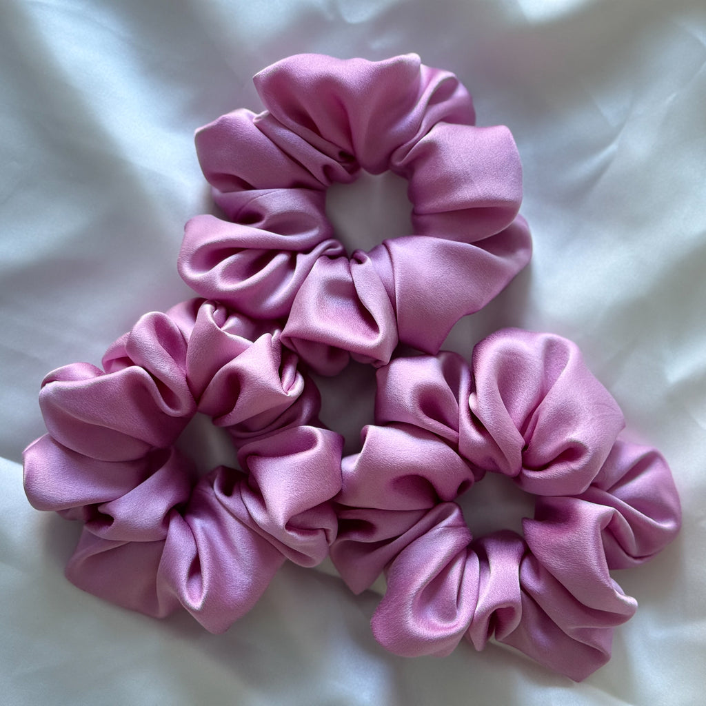 Three pink scrunchies on a white fabric background