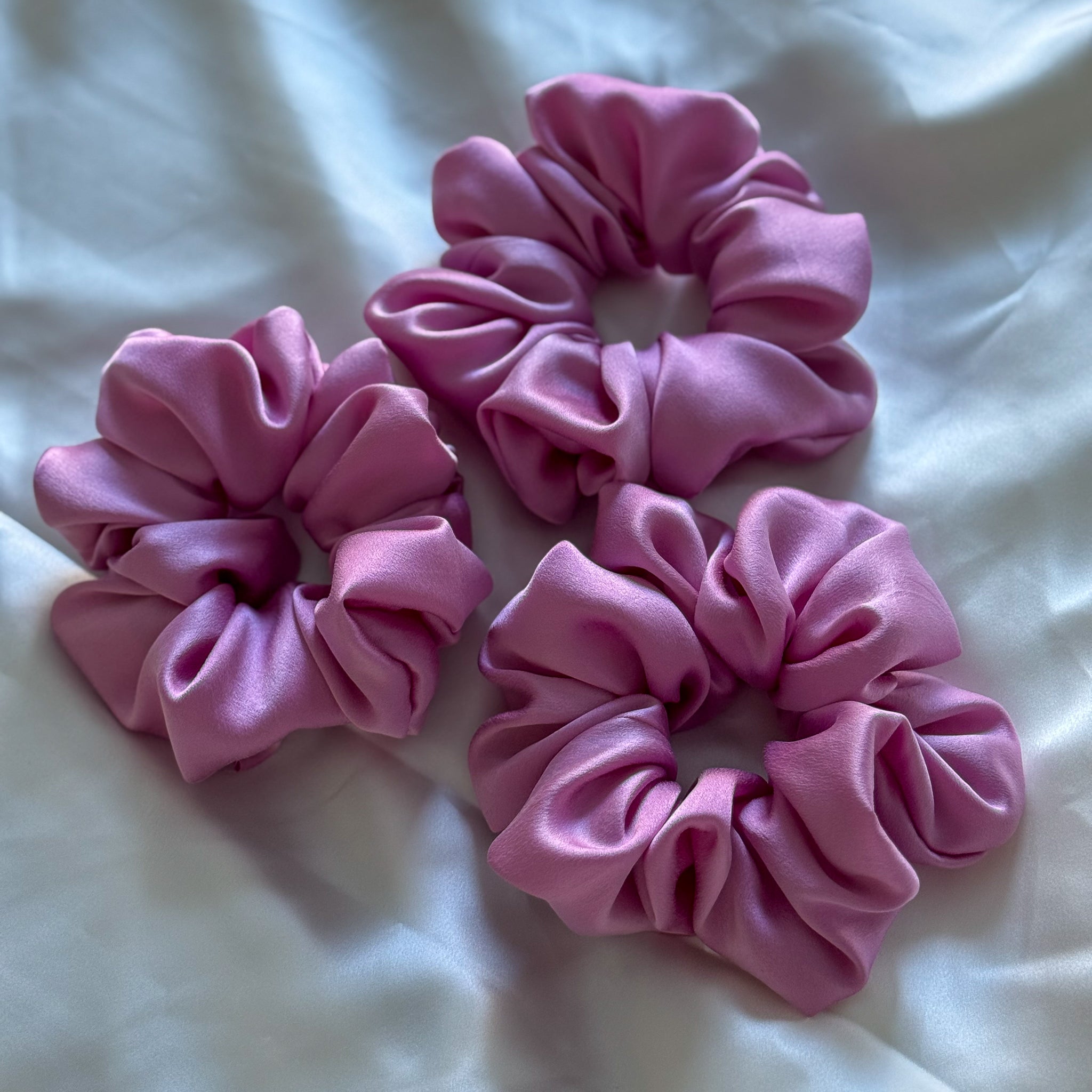 Three large pink scrunchies on a white fabric background