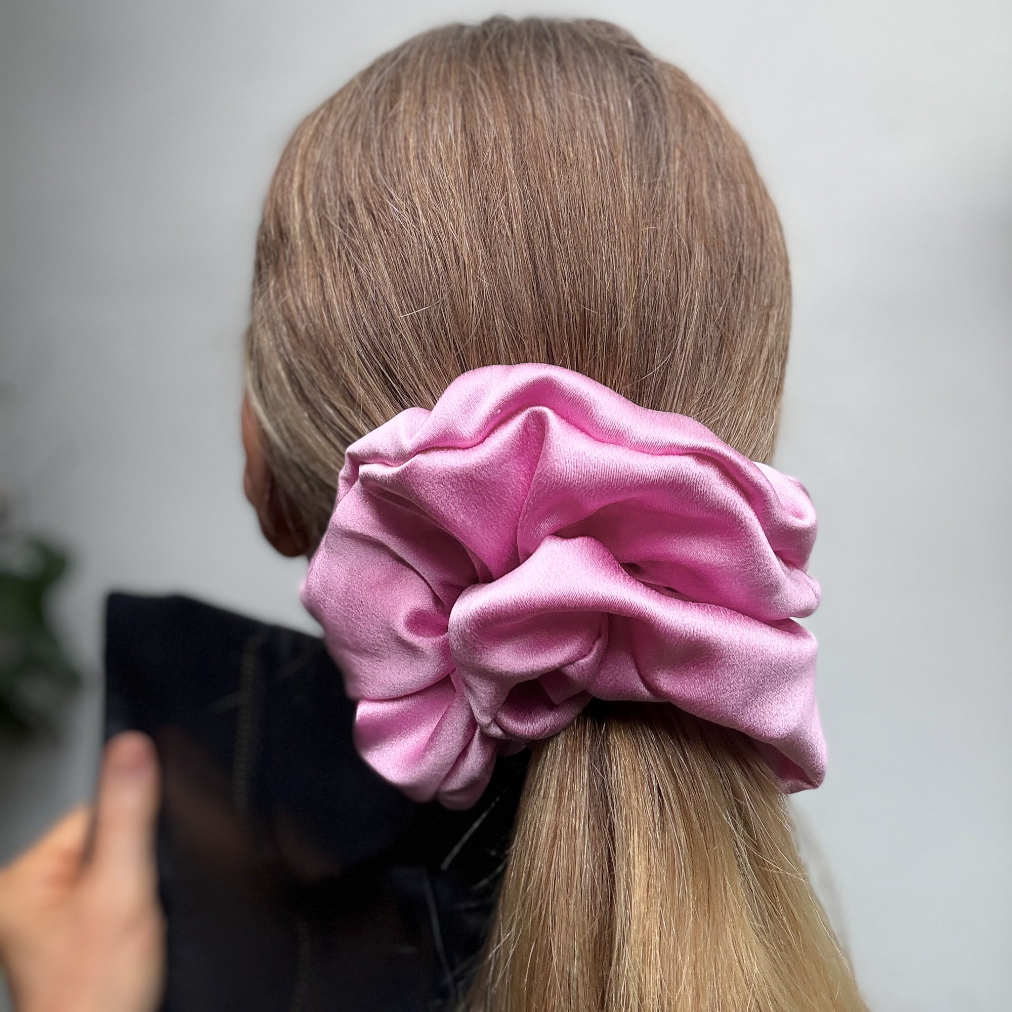Pink scrunchie on a person's hair against a neutral background