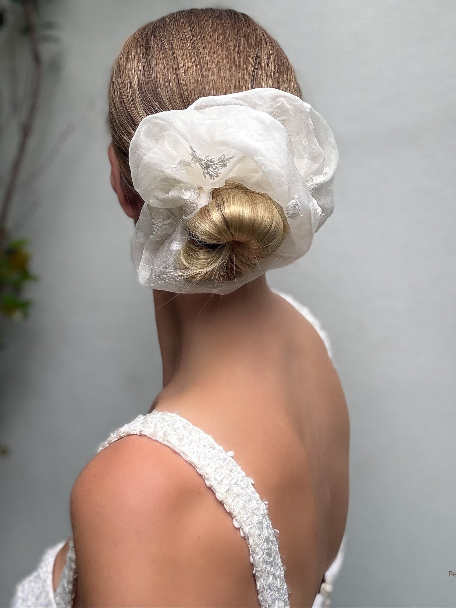Woman with a styled hair bun covered by a white fabric against a neutral background