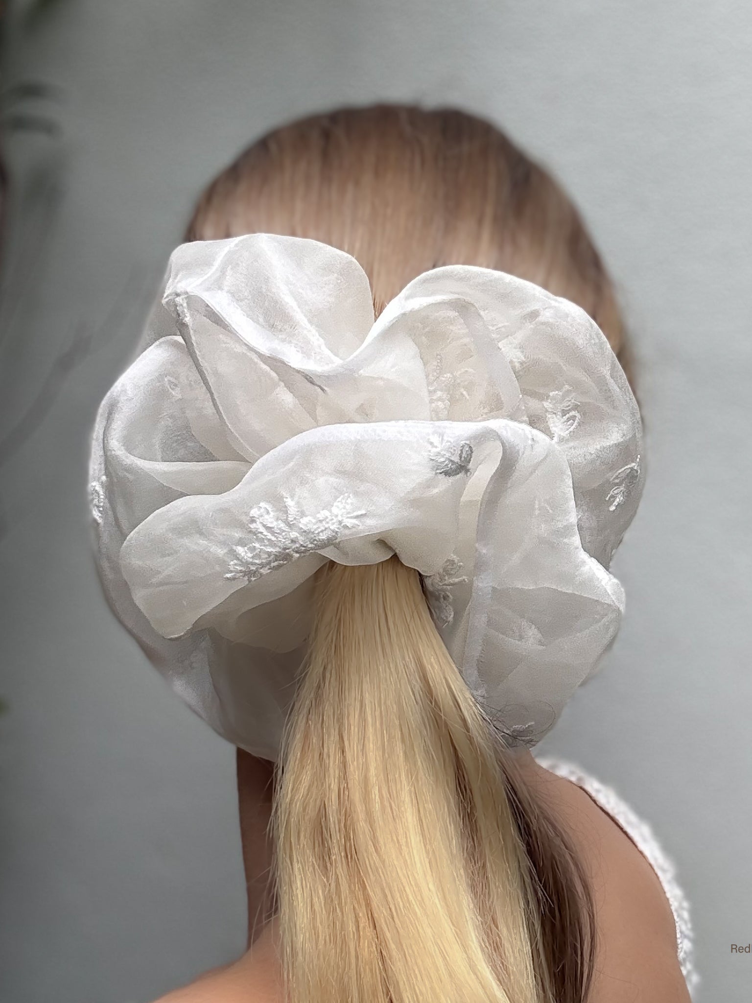 White lace scrunchie on a person's hair against a neutral background