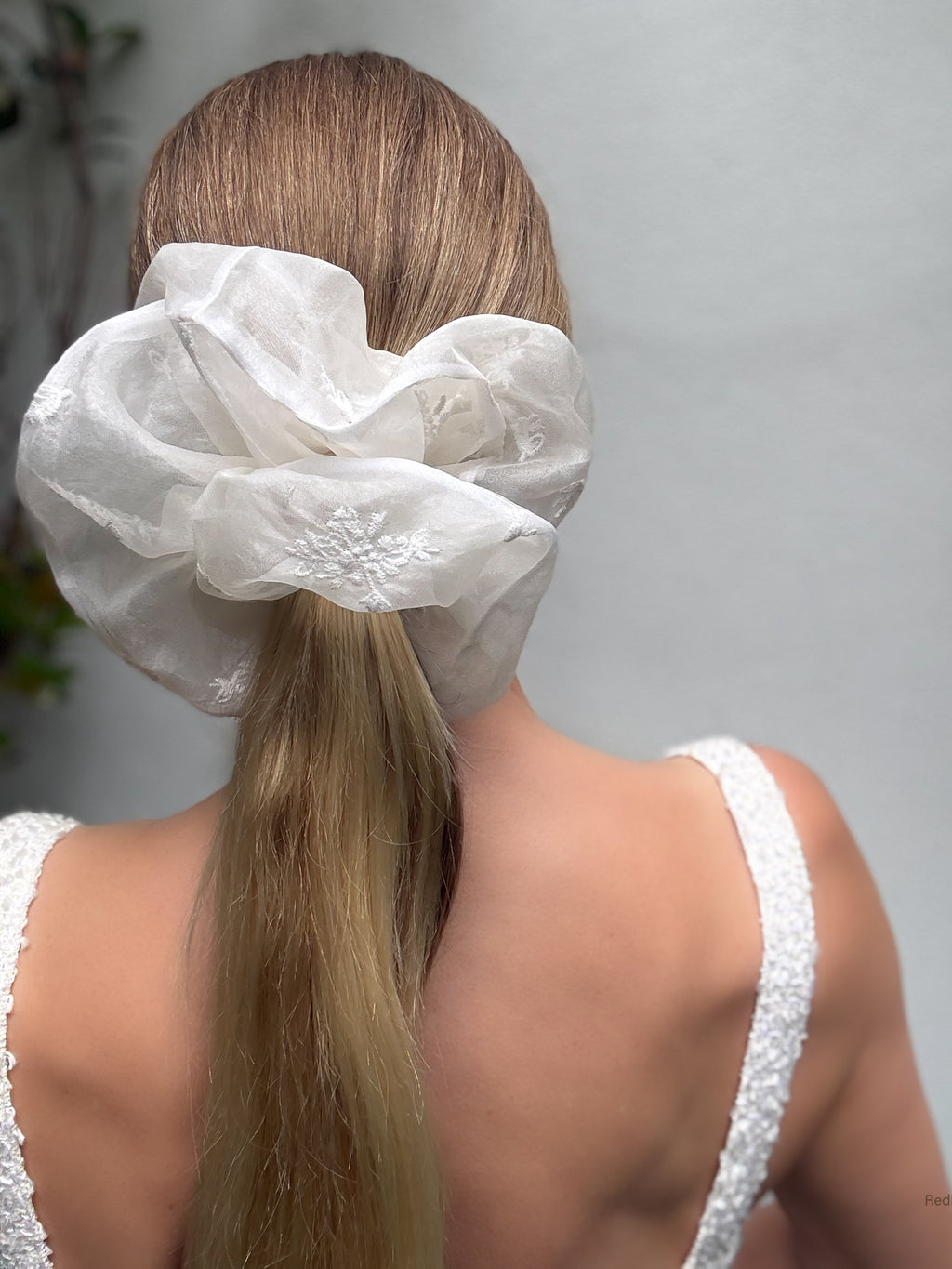 White sheer scrunchie on a person's hair against a neutral background