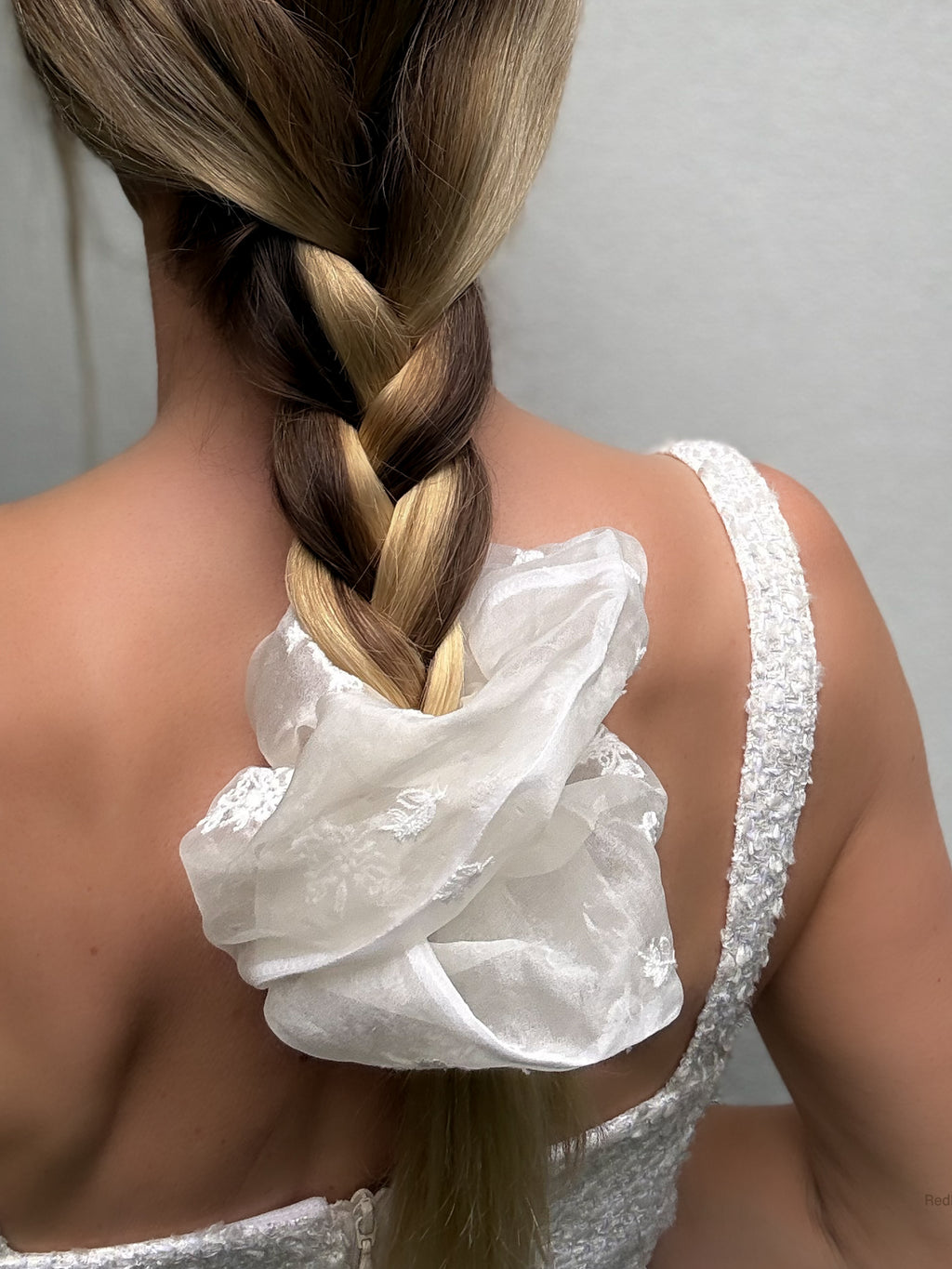 Person wearing a white lace top with a braided hairstyle on a plain background