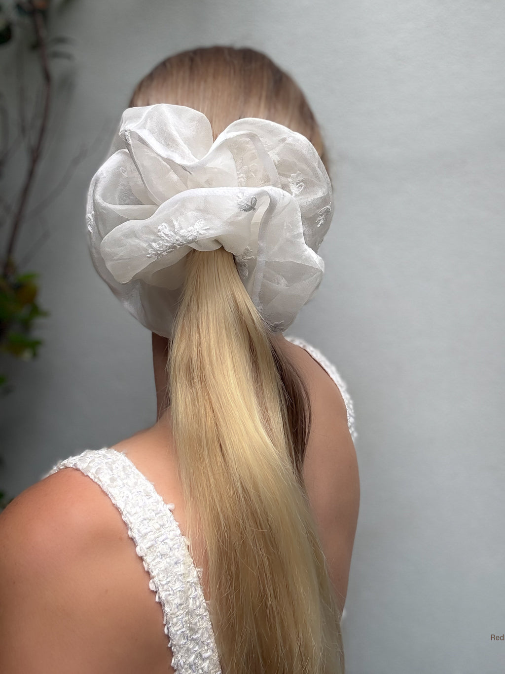 Person with a white lace hair scrunchie in their hair against a neutral background