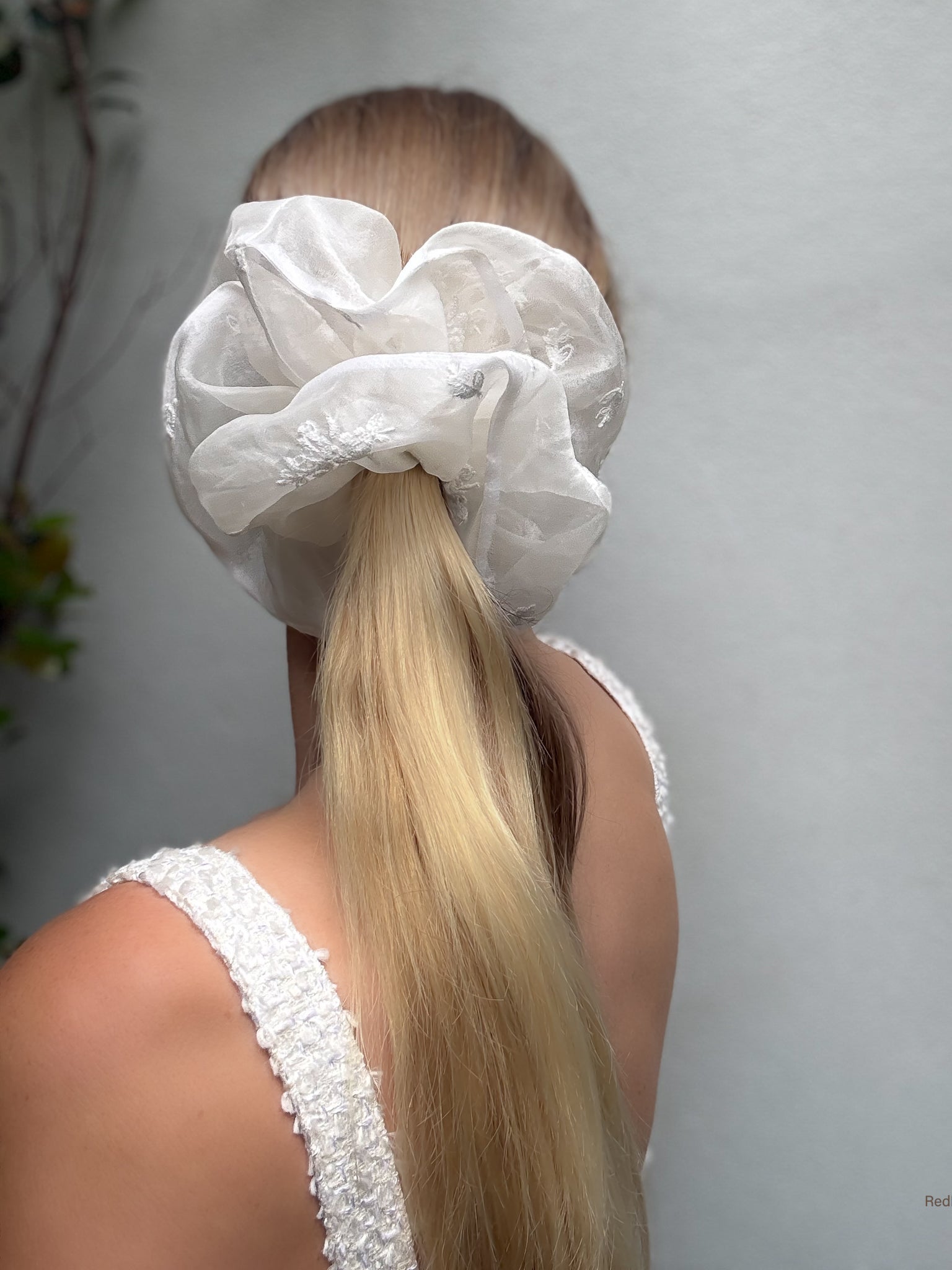 Person with a white lace hair scrunchie in their hair against a neutral background
