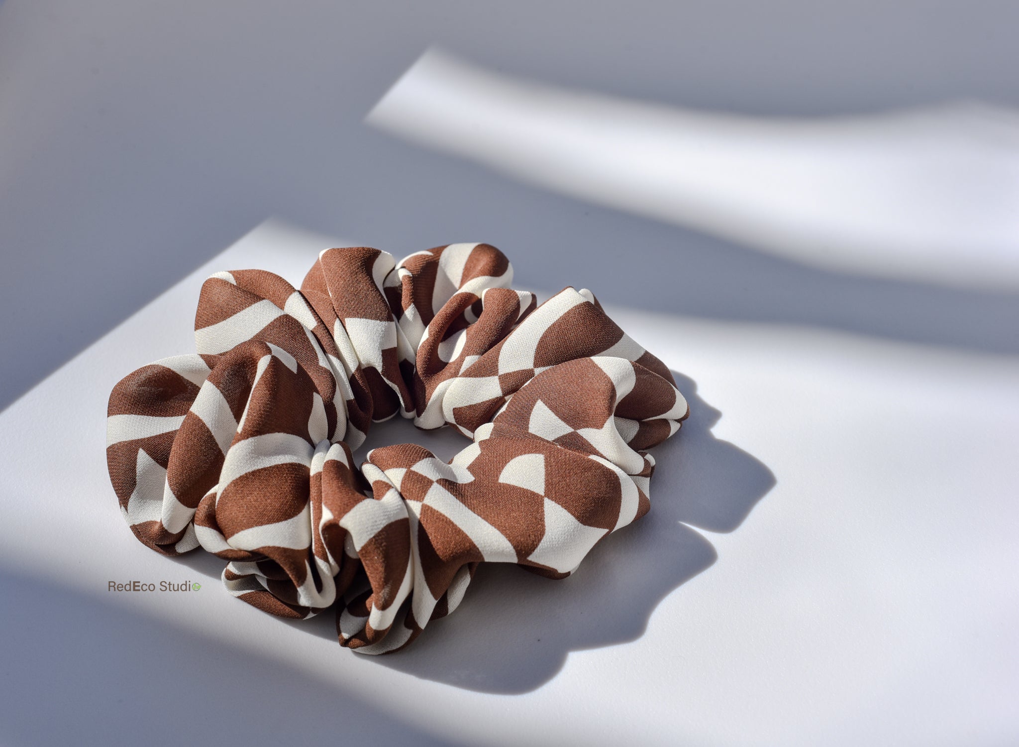Brown and white patterned silk scrunchie on a light surface