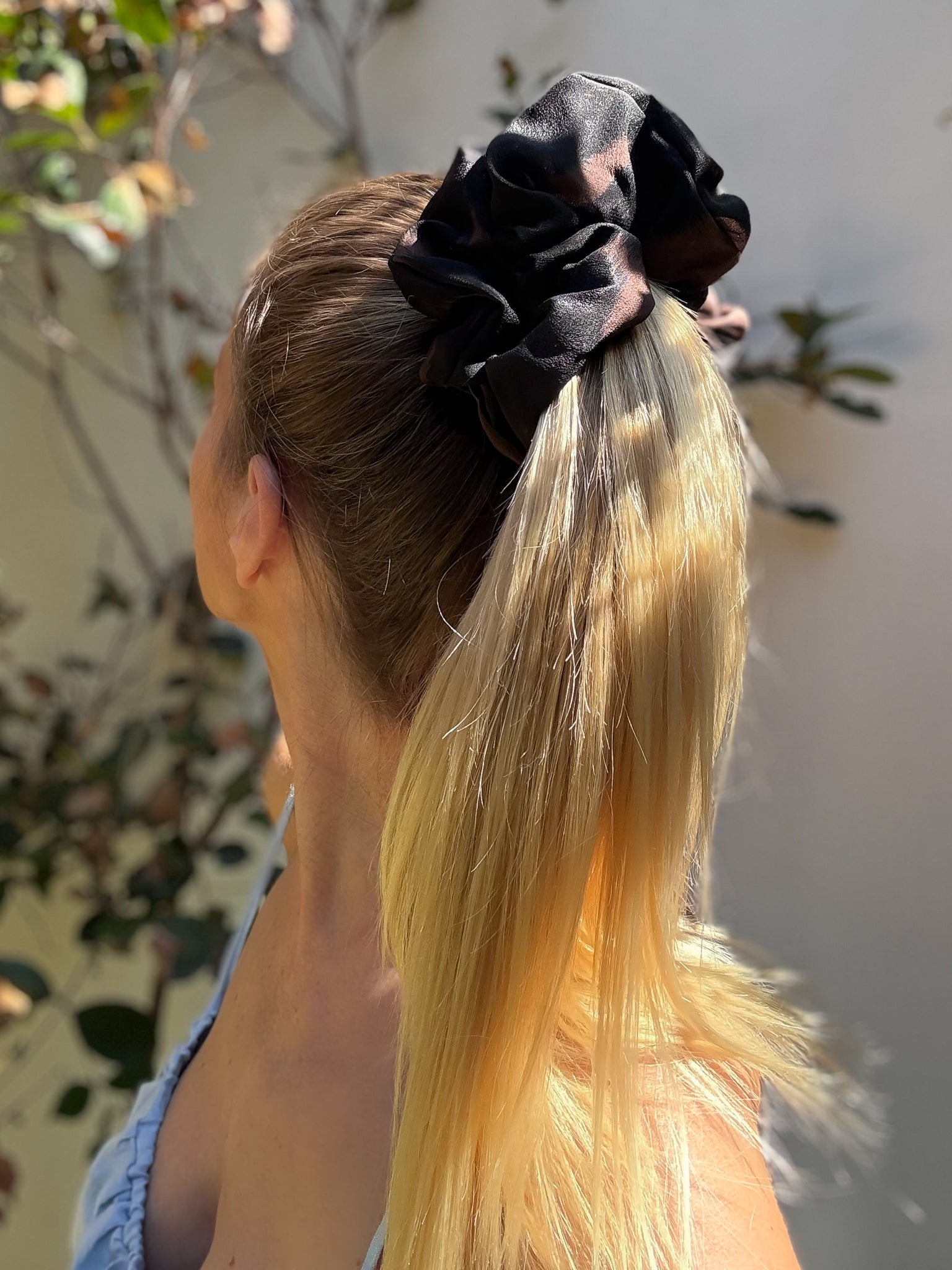 Person with blonde hair tied back with a black scrunchie, outdoor setting