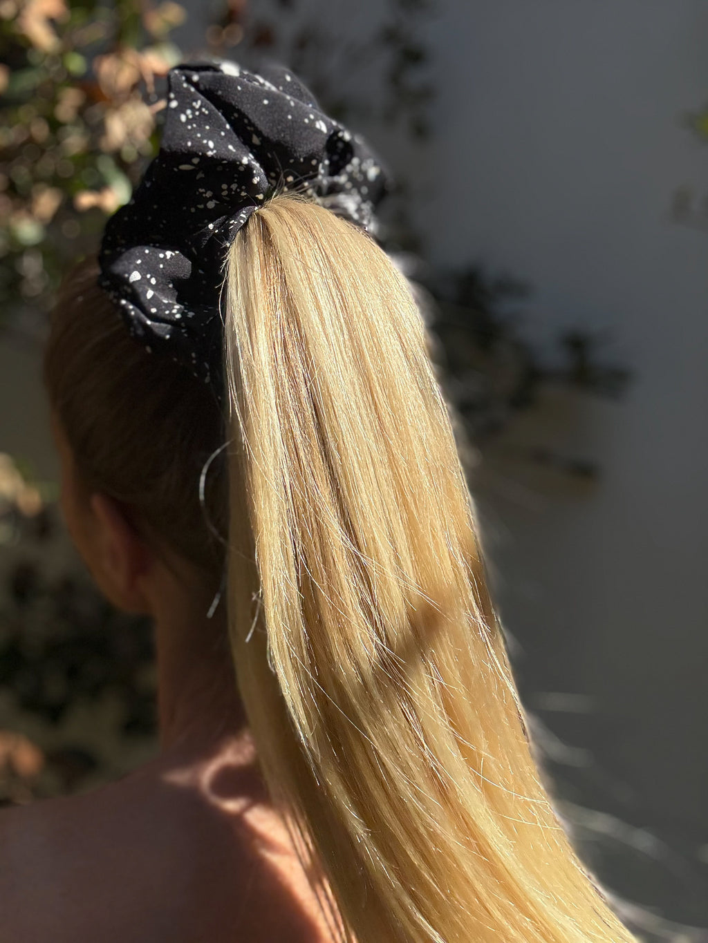 Person with long blonde hair wearing a black extra large scrunchie outdoors.