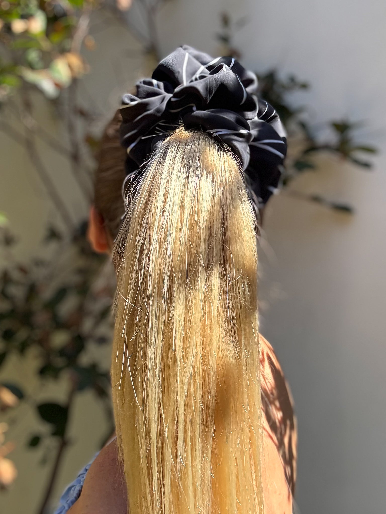 Black scrunchie on blonde hair with a blurred outdoor background
