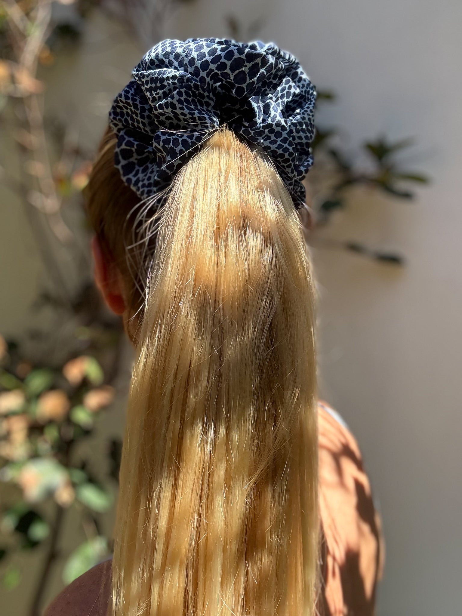 Person with blue patterned scrunchie in blonde hair, outdoor setting