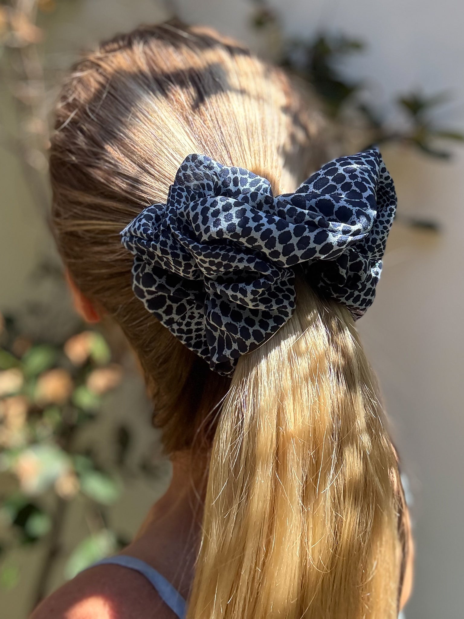 Person with blonde hair tied back with a blue leopard print hair bow.