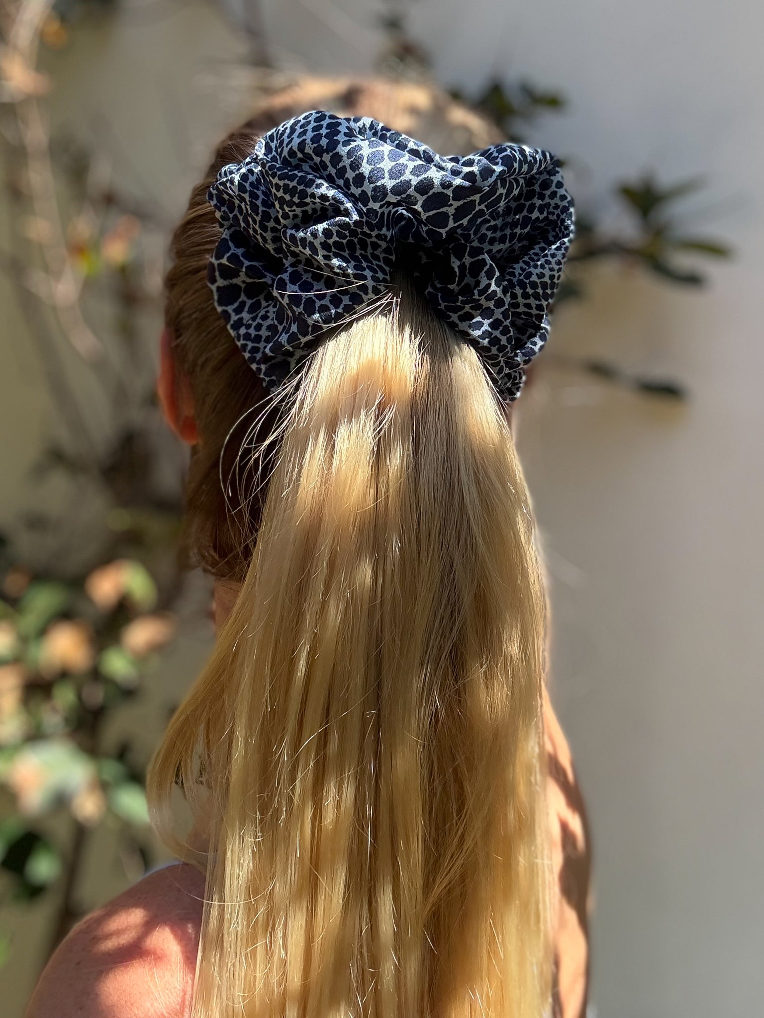 Person with blonde hair tied with a blue and white patterned hair tie against a blurred natural background