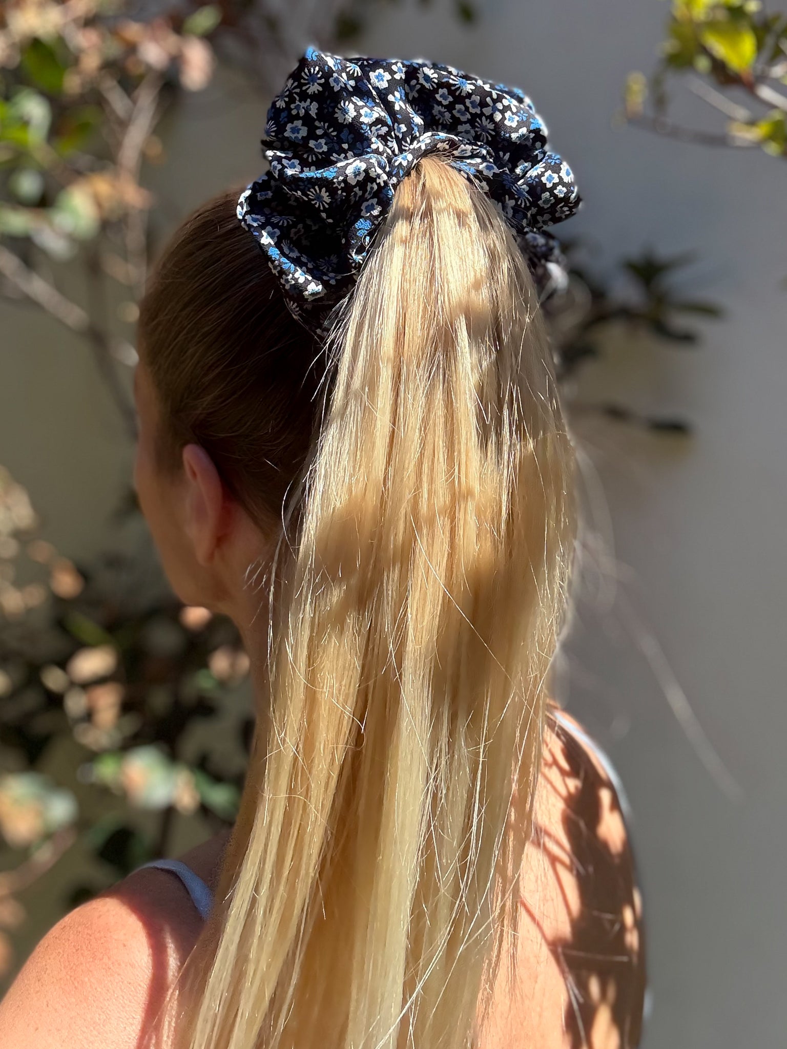 Person with long blonde hair wearing a blue floral scrunchie.