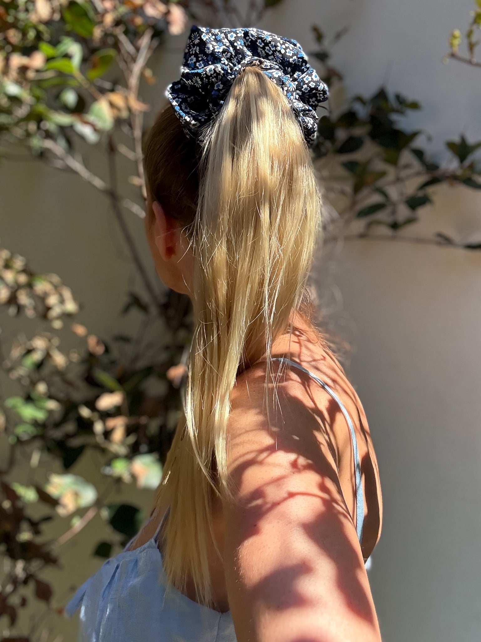 Person with blonde hair tied in a ponytail with a blue scrunchie, wearing a blue dress.