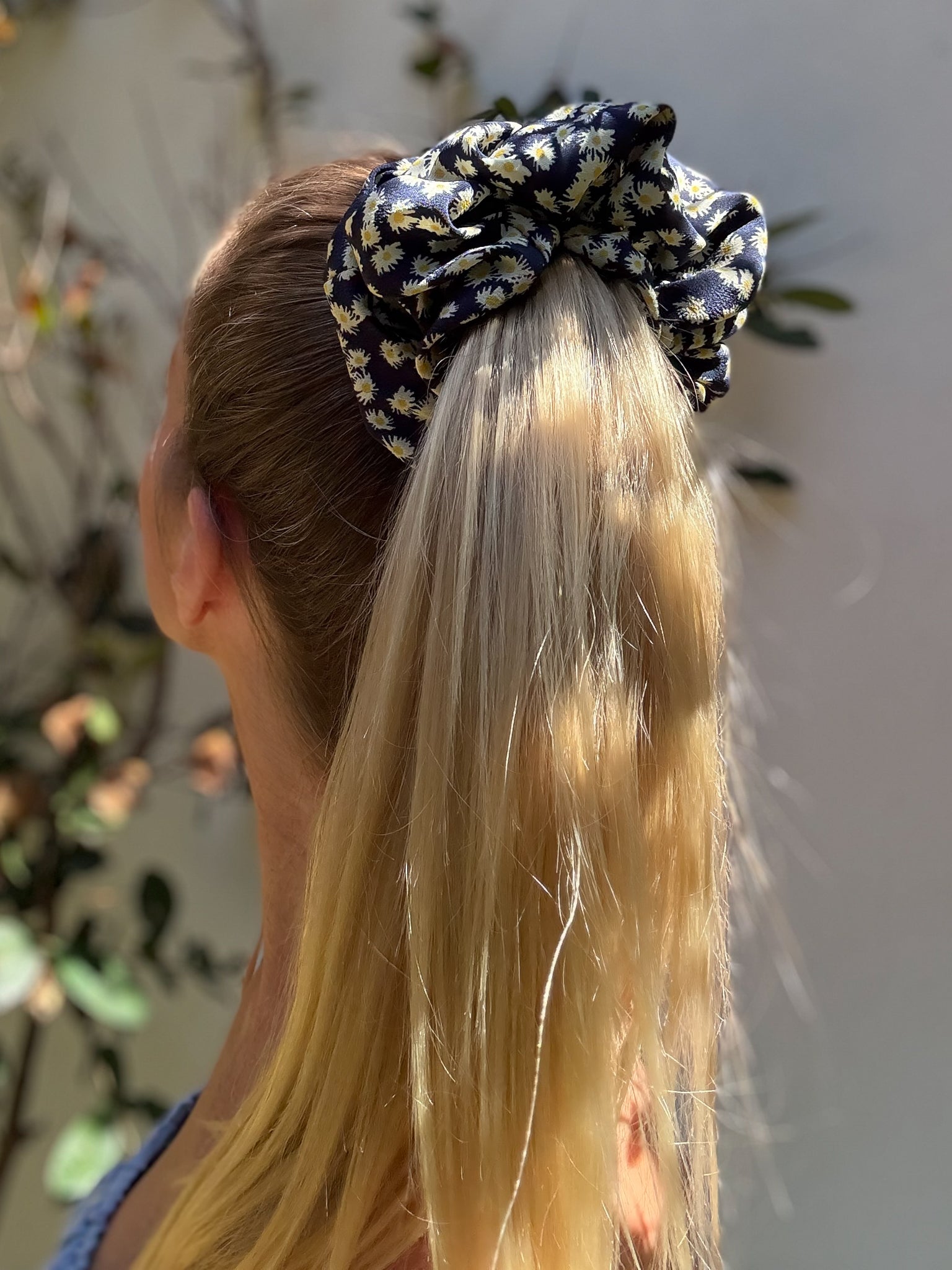 Person with a patterned scrunchie in their hair against a blurred natural background