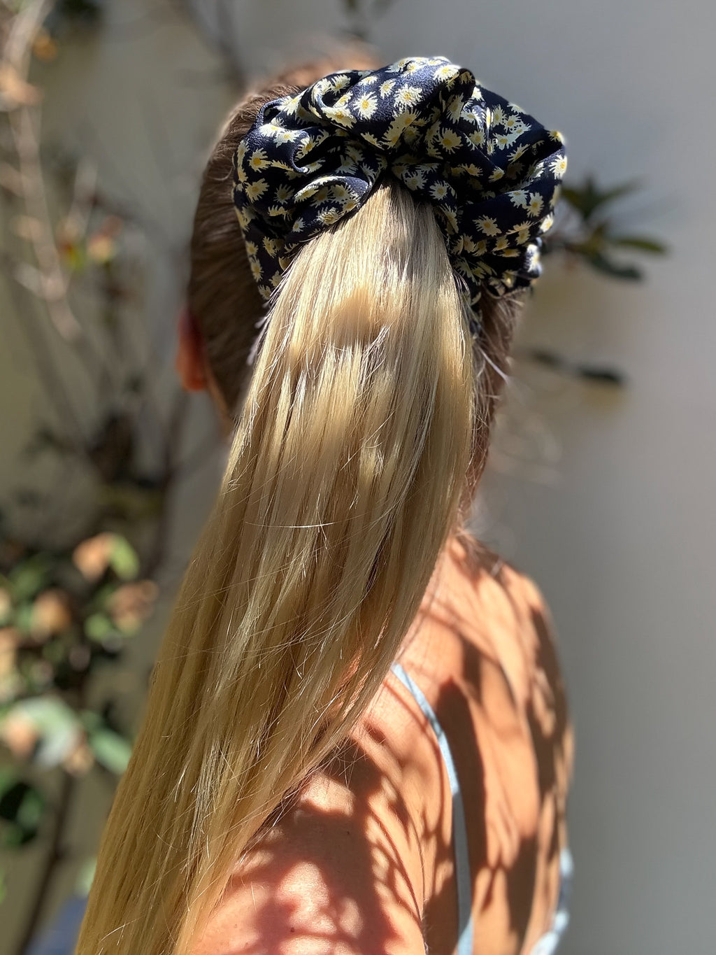 Person with long blonde hair tied up with a patterned scrunchie against a blurred outdoor background