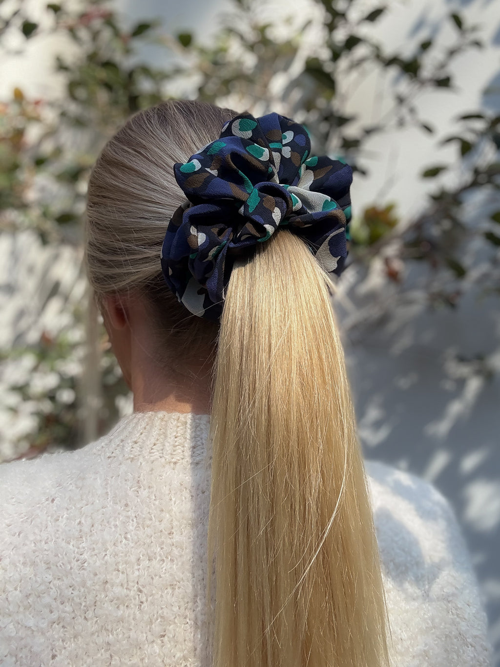 Woman with a high ponytail wearing a silk scrunchie against a blurred natural background
