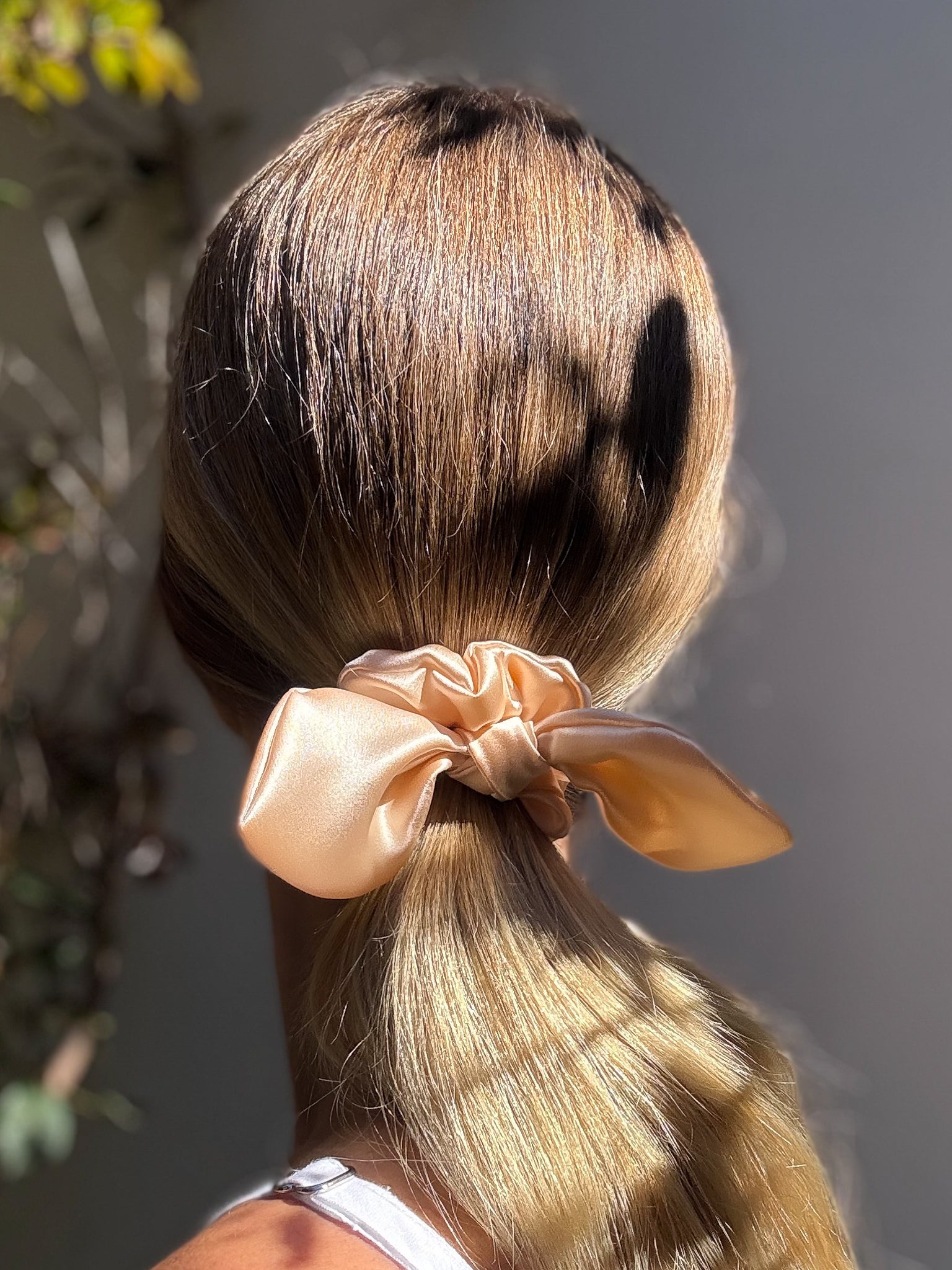 Blonde hair tied with a pink scrunchie against a neutral background