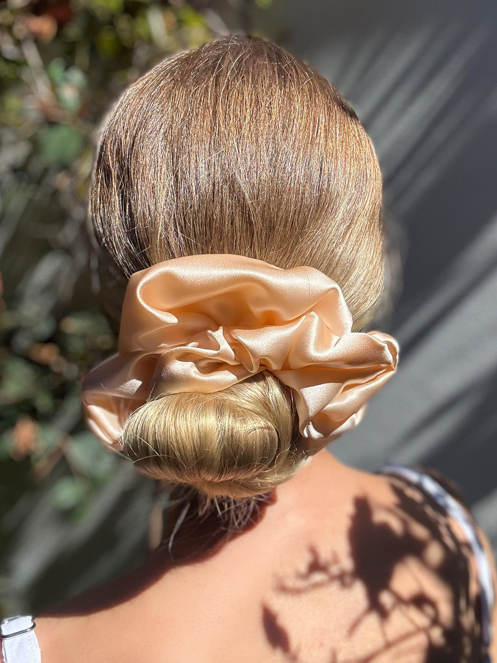 Person with a bun holding a beige scrunchie against a blurred natural background