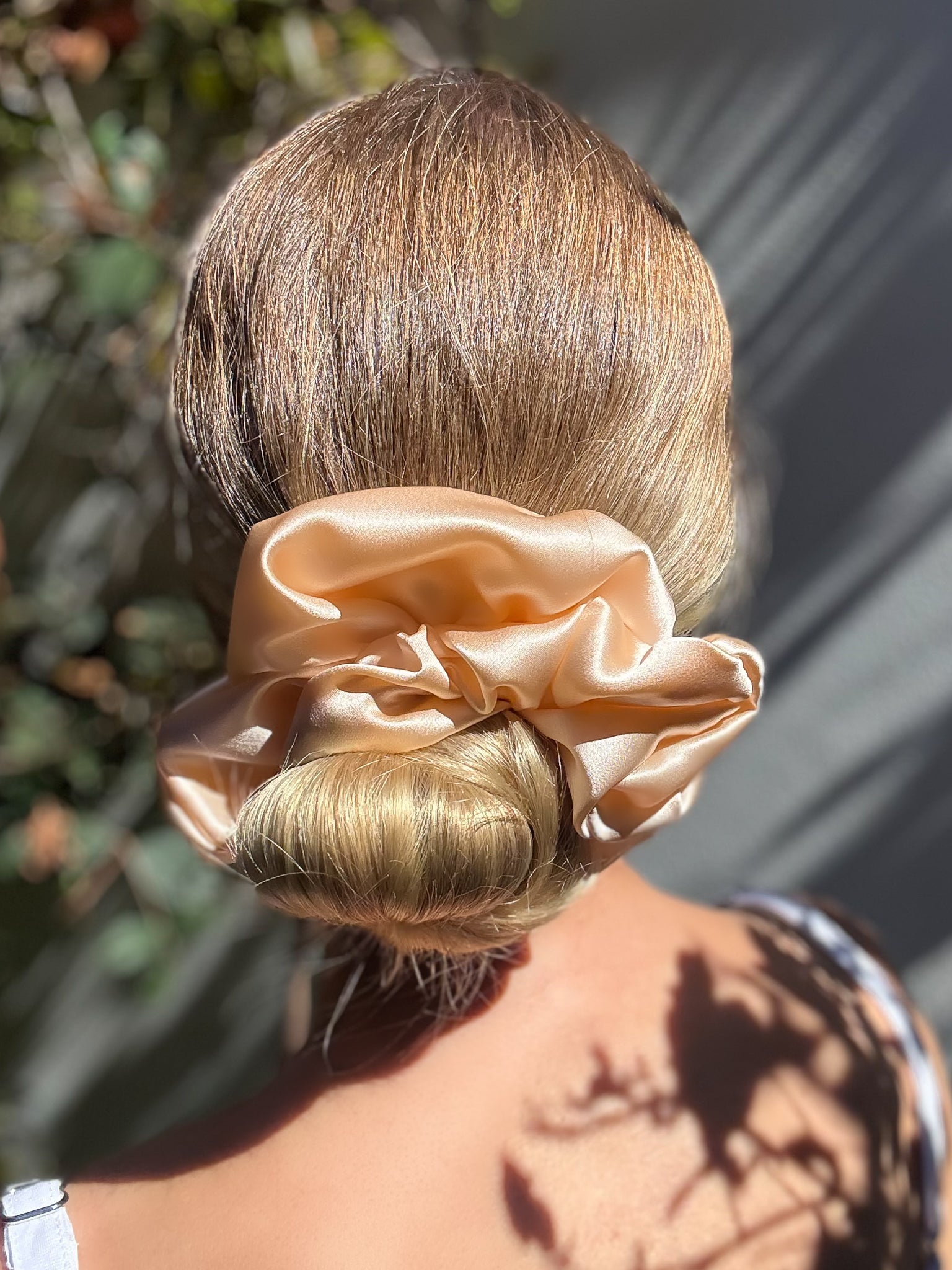 Person with a bun holding a beige scrunchie against a blurred natural background