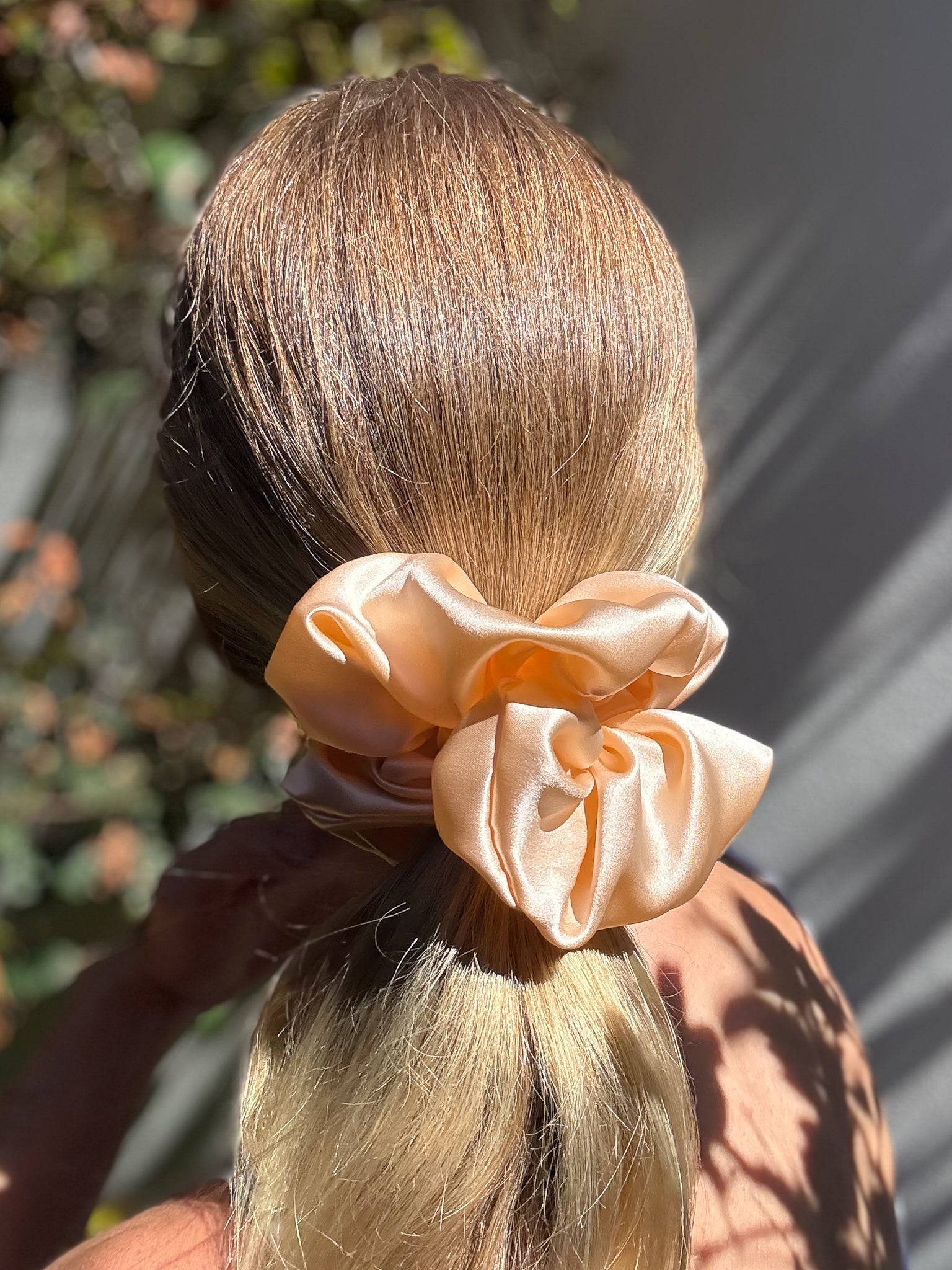 Blonde hair tied with a large peach scrunchie against a blurred natural background
