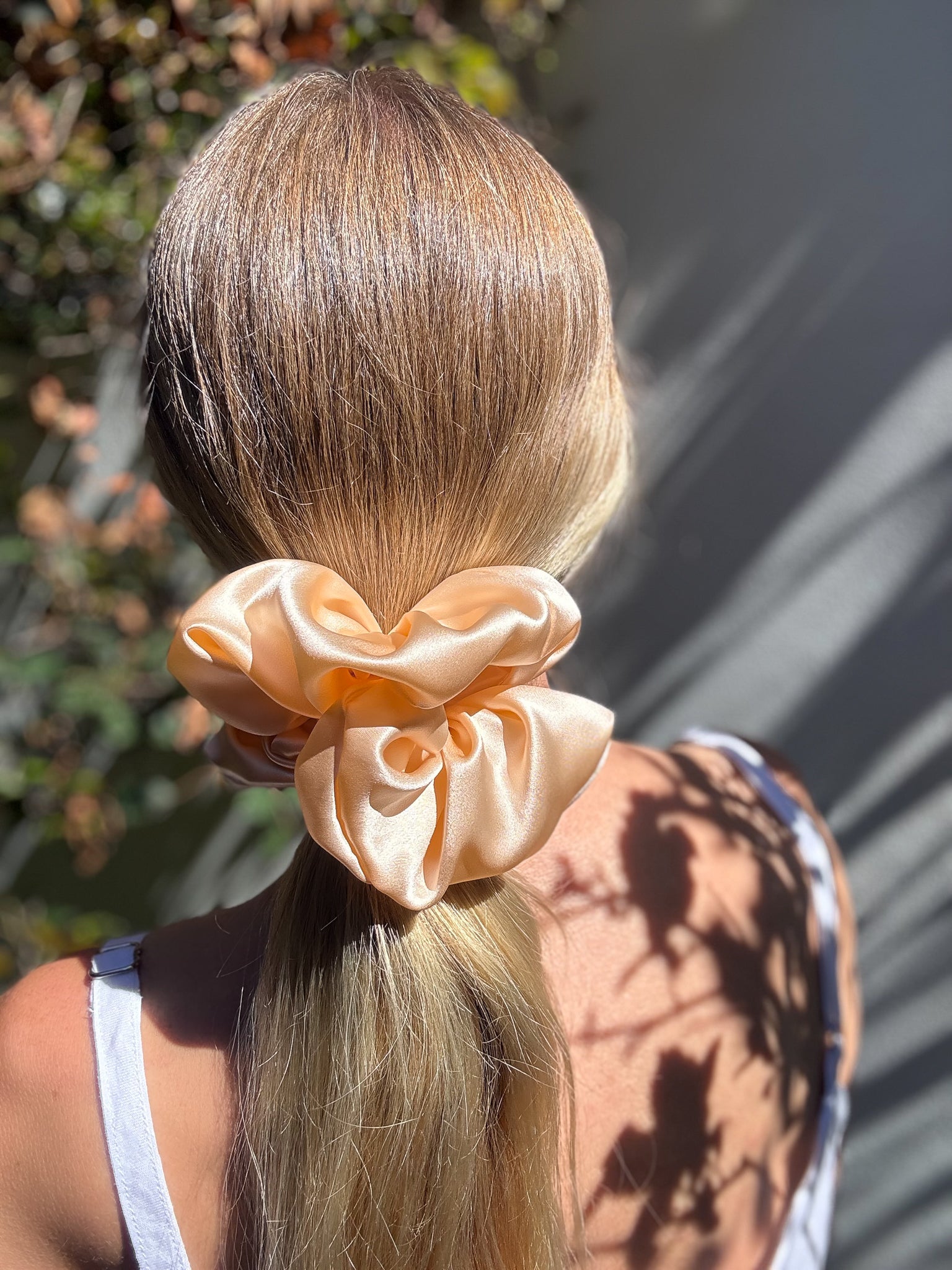 Person with blonde hair tied in a ponytail with an orange scrunchie, outdoors.