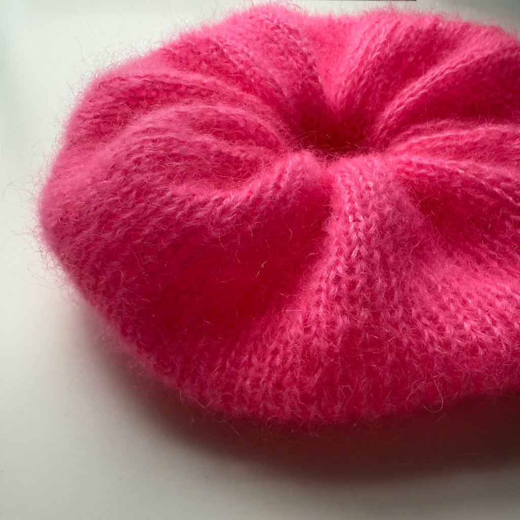 Close up of an extra large pink knitted scrunchie on a white background