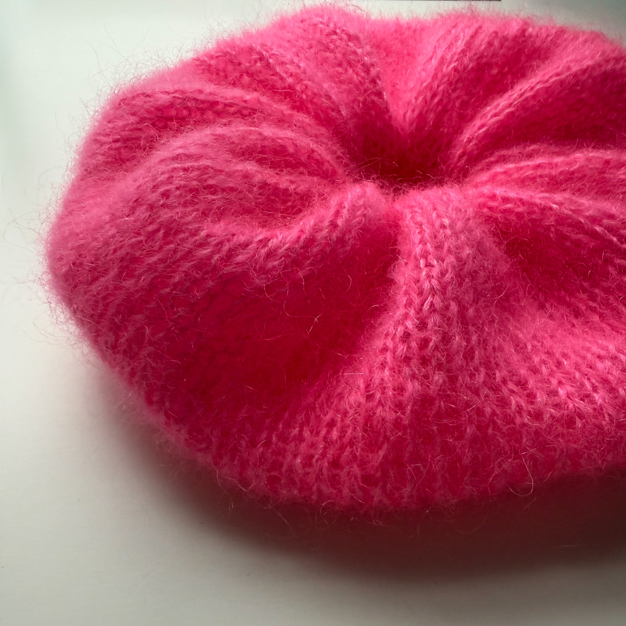 Close up of an extra large pink knitted scrunchie on a white background
