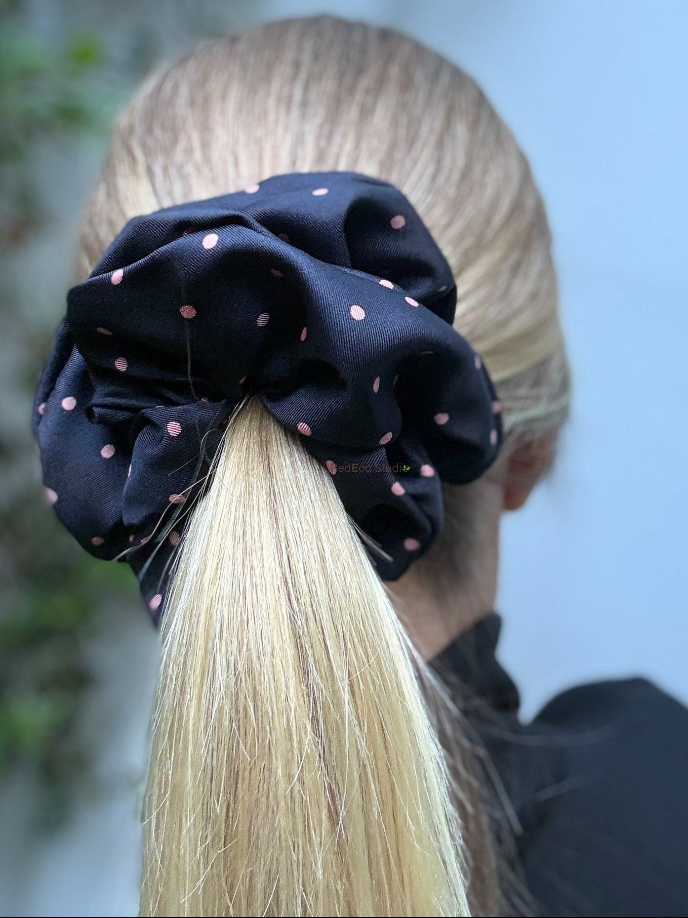 Person with a black polka dot scrunchie on a blonde ponytail against a blurred natural background