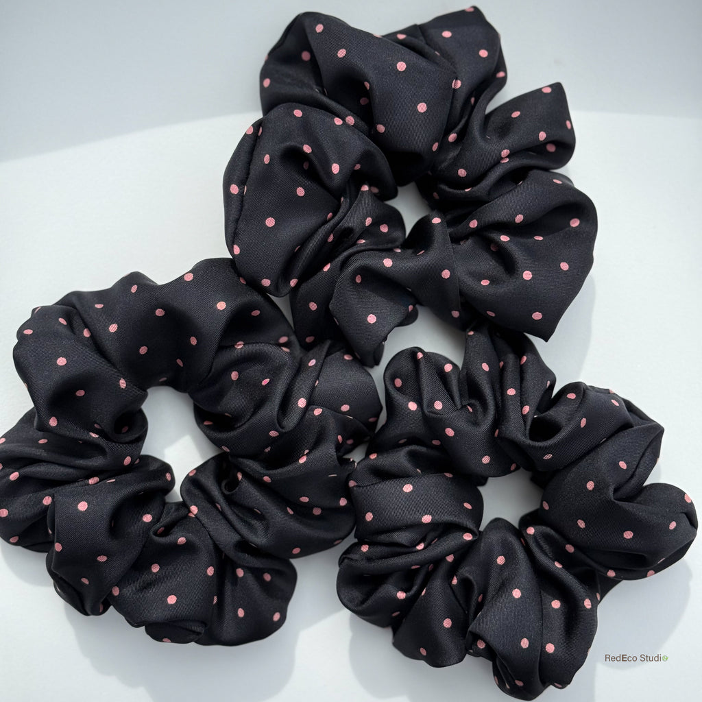 Three black scrunchies with pink polka dots on a white background