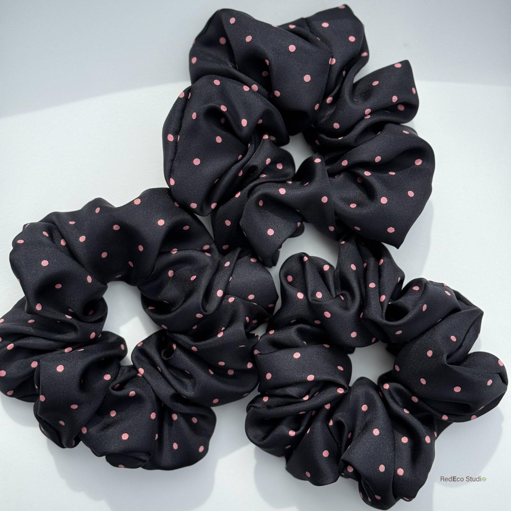 Three black scrunchies with pink polka dots on a white background