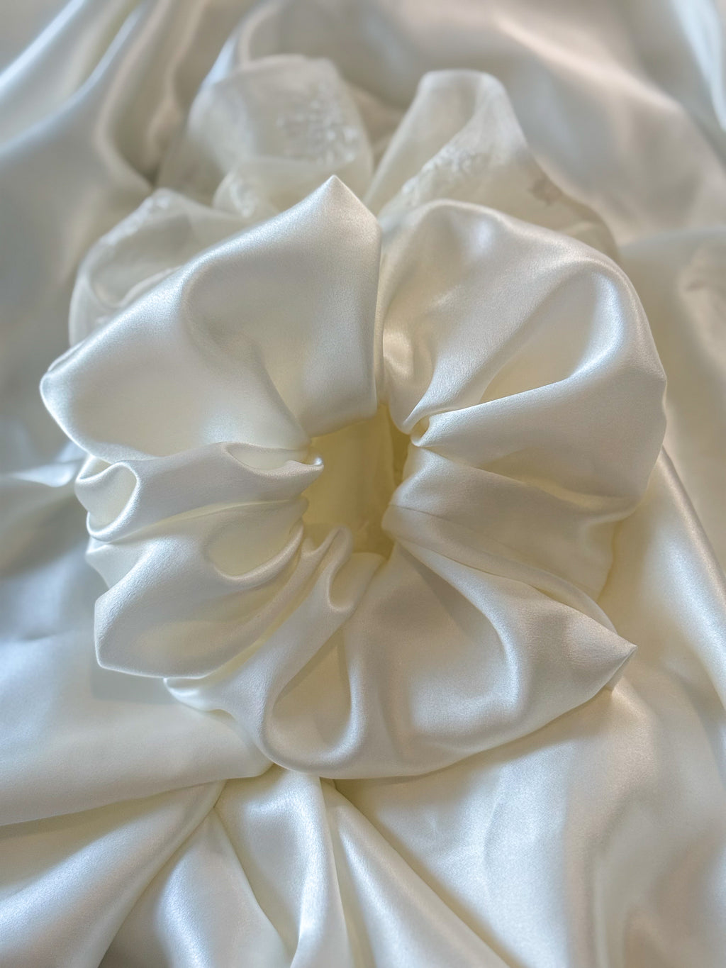Close-up of a white satin hair scrunchie on a white fabric background