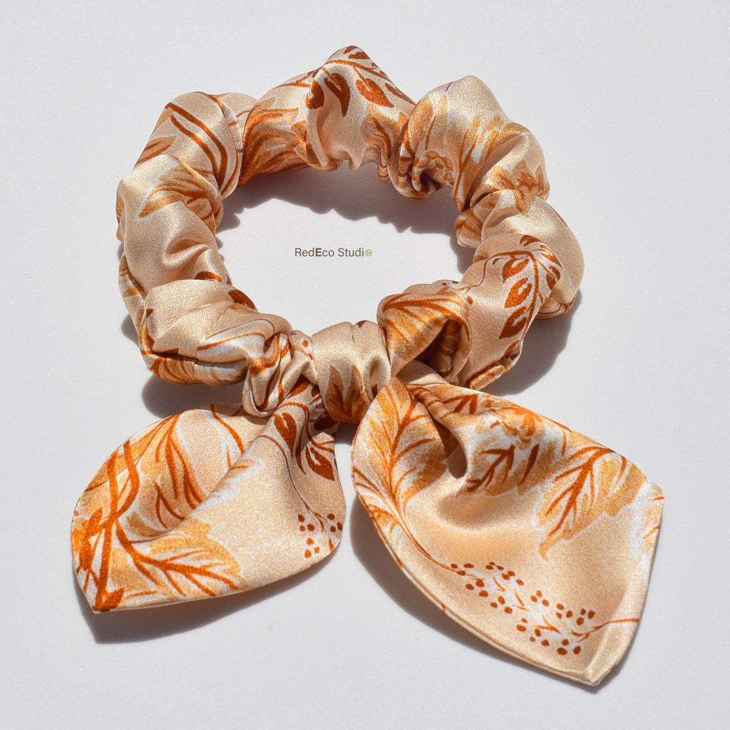 Silk bow scrunchie with orange floral pattern on a white background