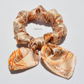 Silk bow scrunchie with orange floral pattern on a white background