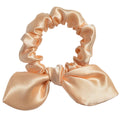 Pink satin scrunchie with a bow on a light gray background
