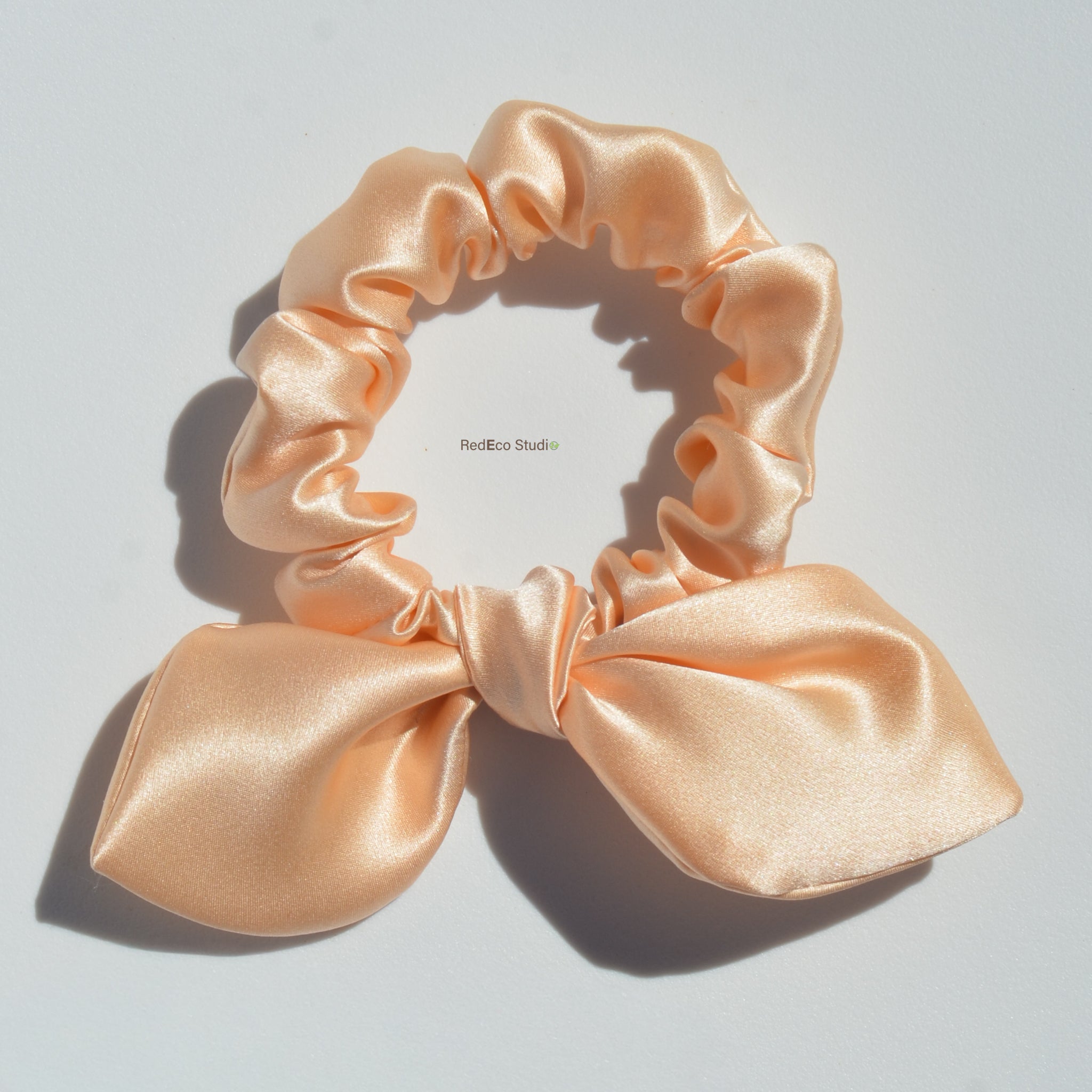 Pink satin scrunchie with a bow on a light gray background