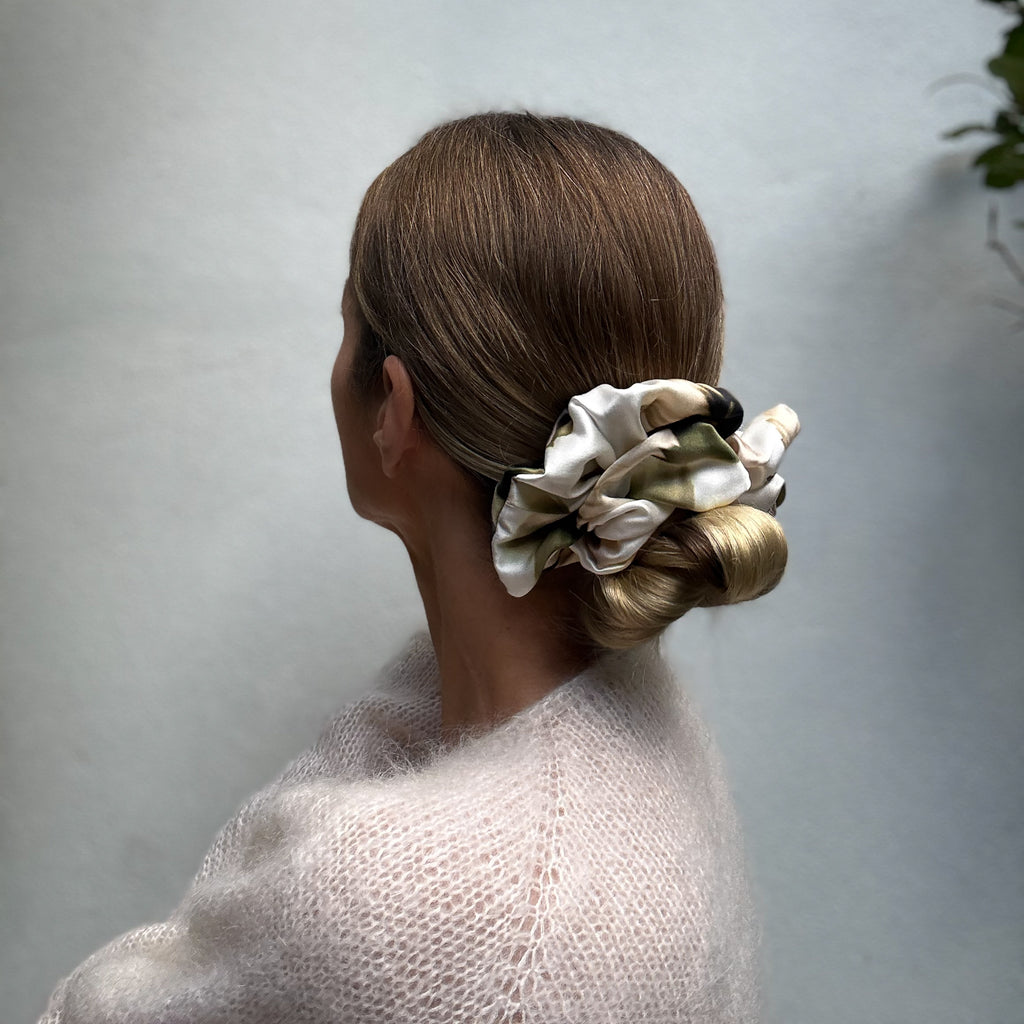 Woman with hair styled in a bun using a patterned scrunchie against a plain background