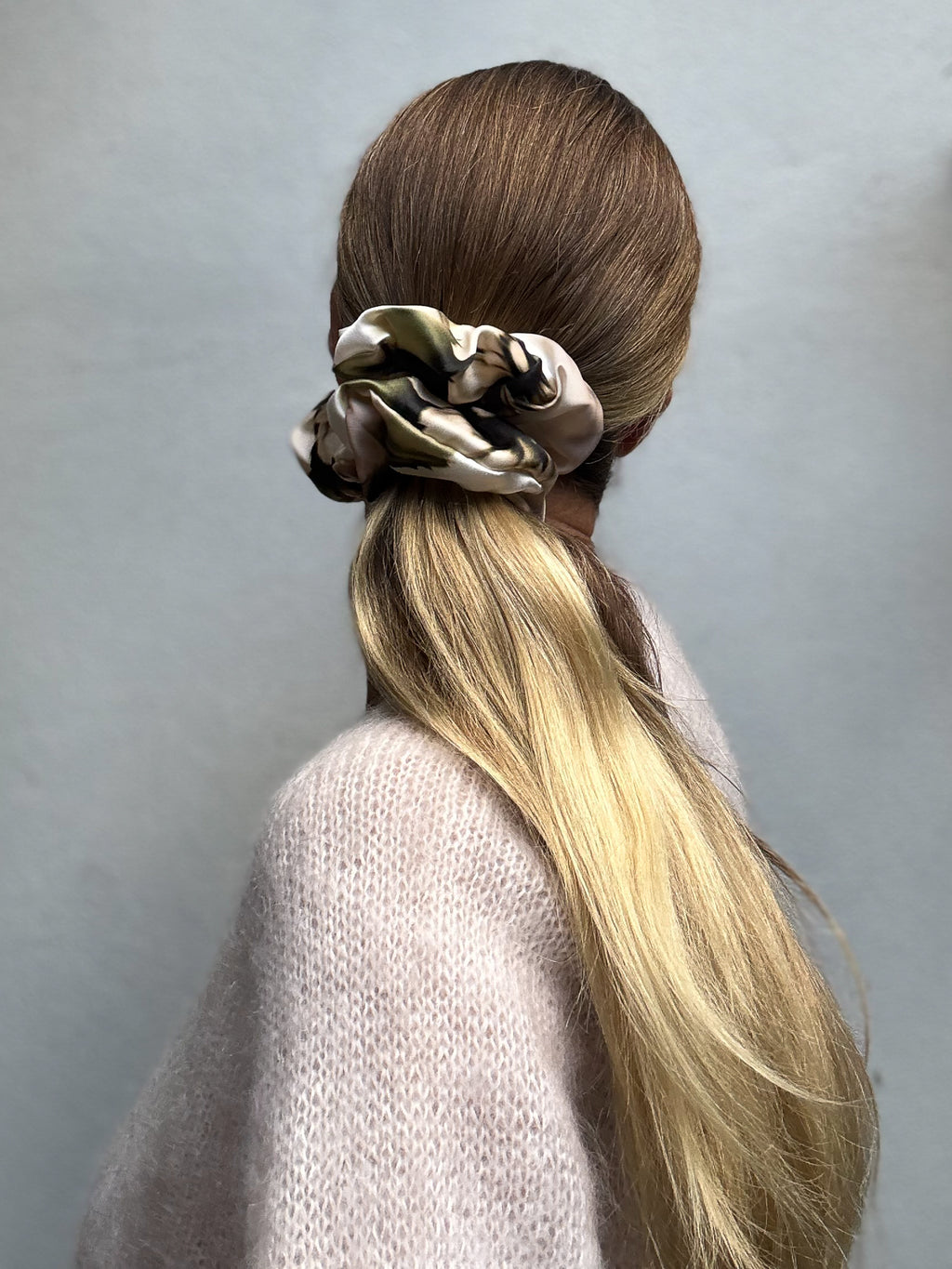 Person with a large silk scrunchie in their hair against a plain background