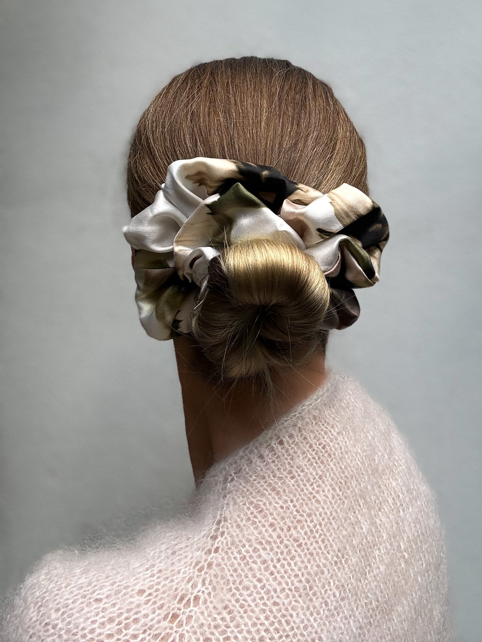 Woman with a bun wearing floral silk scrunchies against a plain background