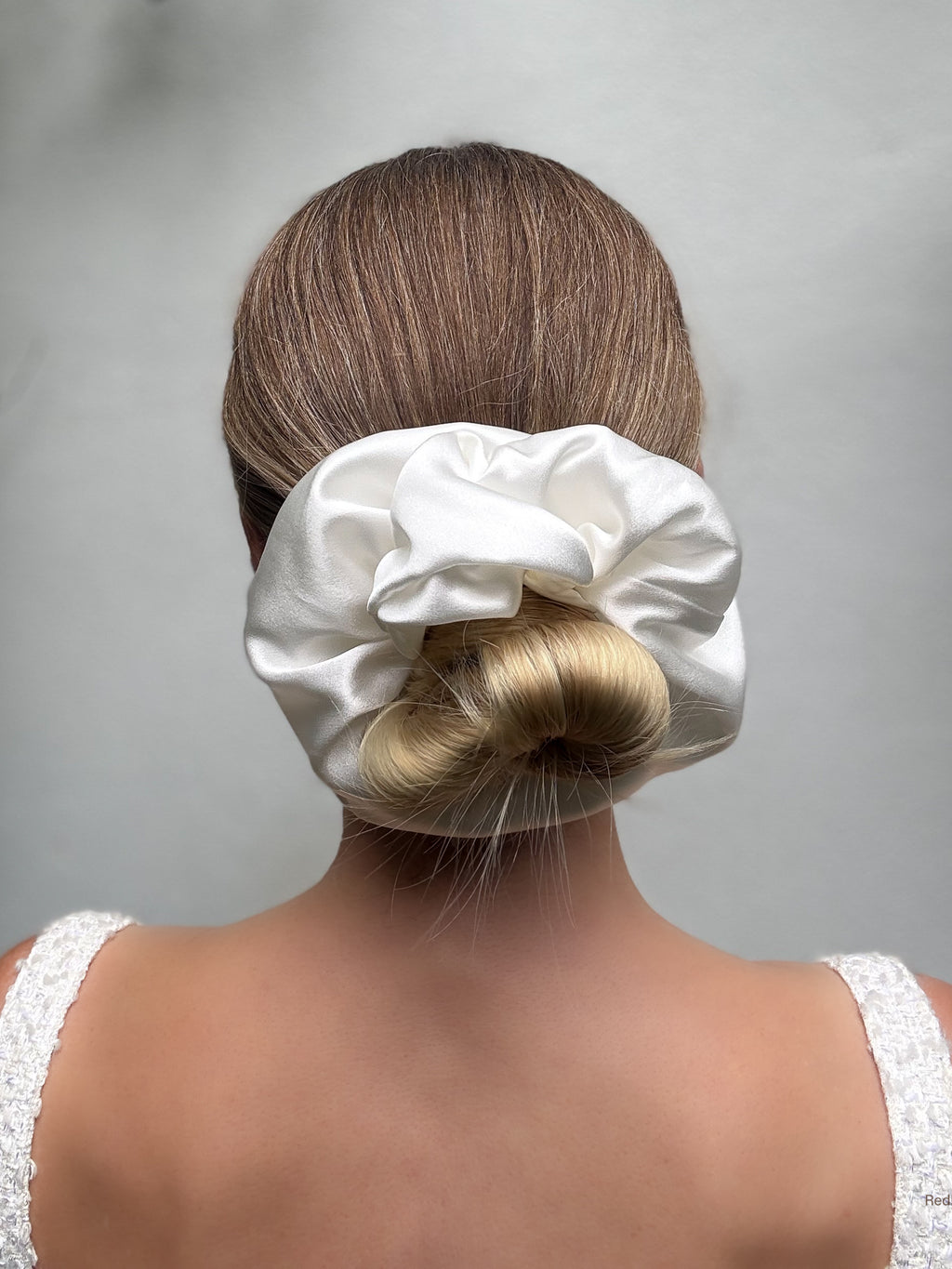 White satin hair scrunchie on a bun against a gray background