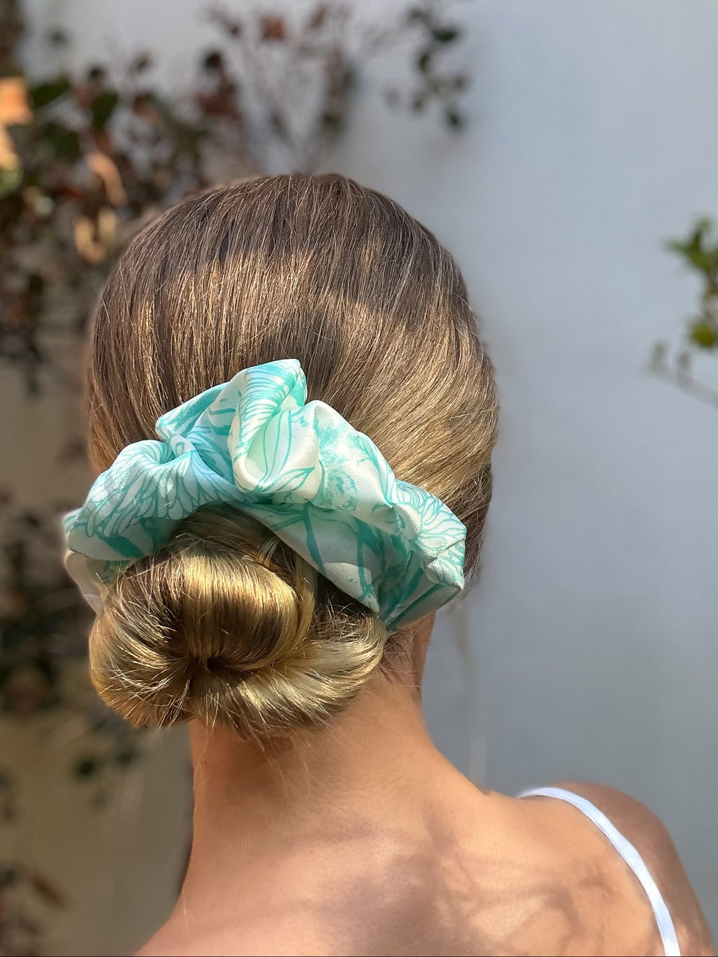 Person with a bun wearing a green scrunchie against a neutral background