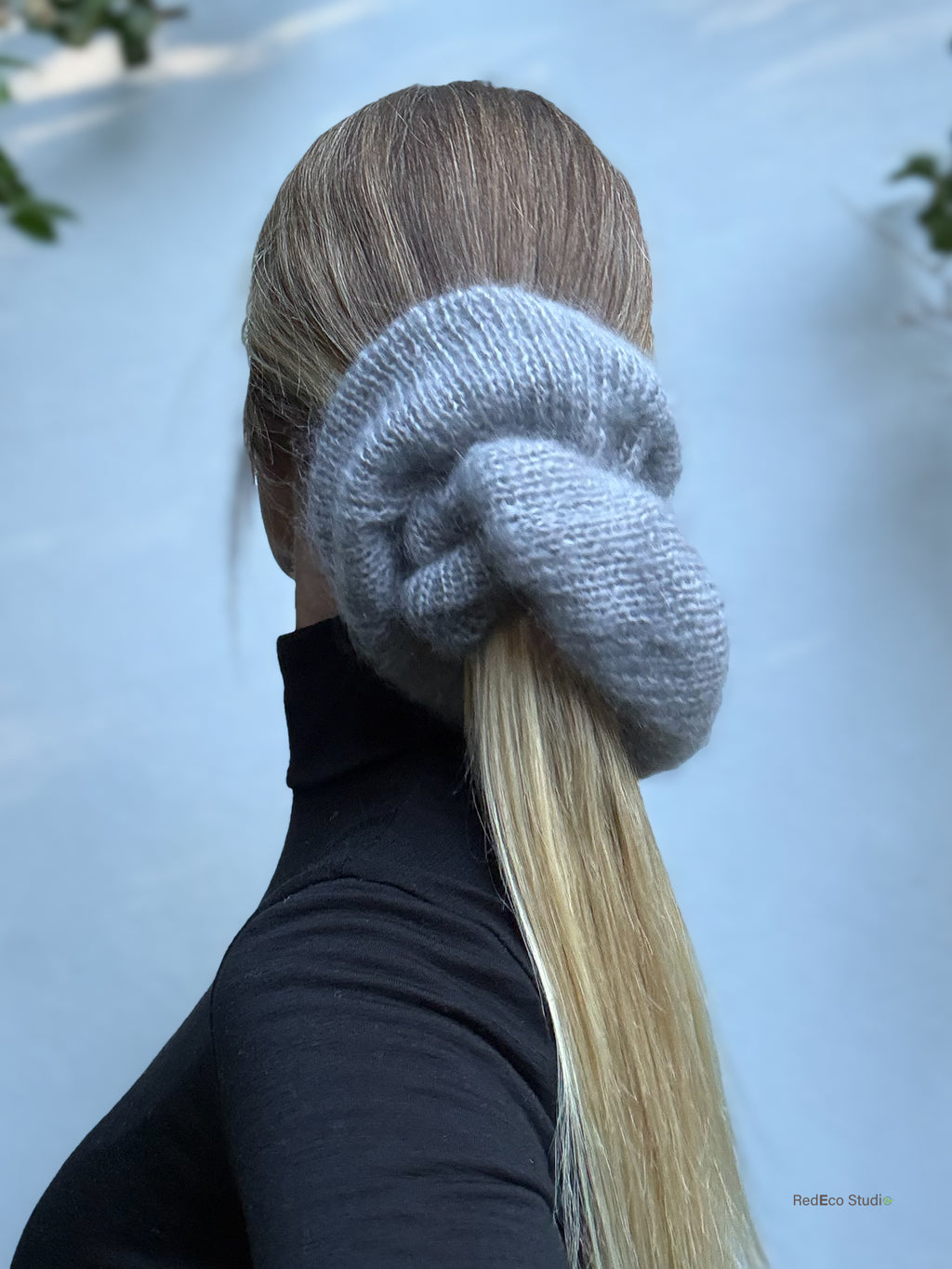 Person with a knitted gray scrunchie on their hair against a light blue background