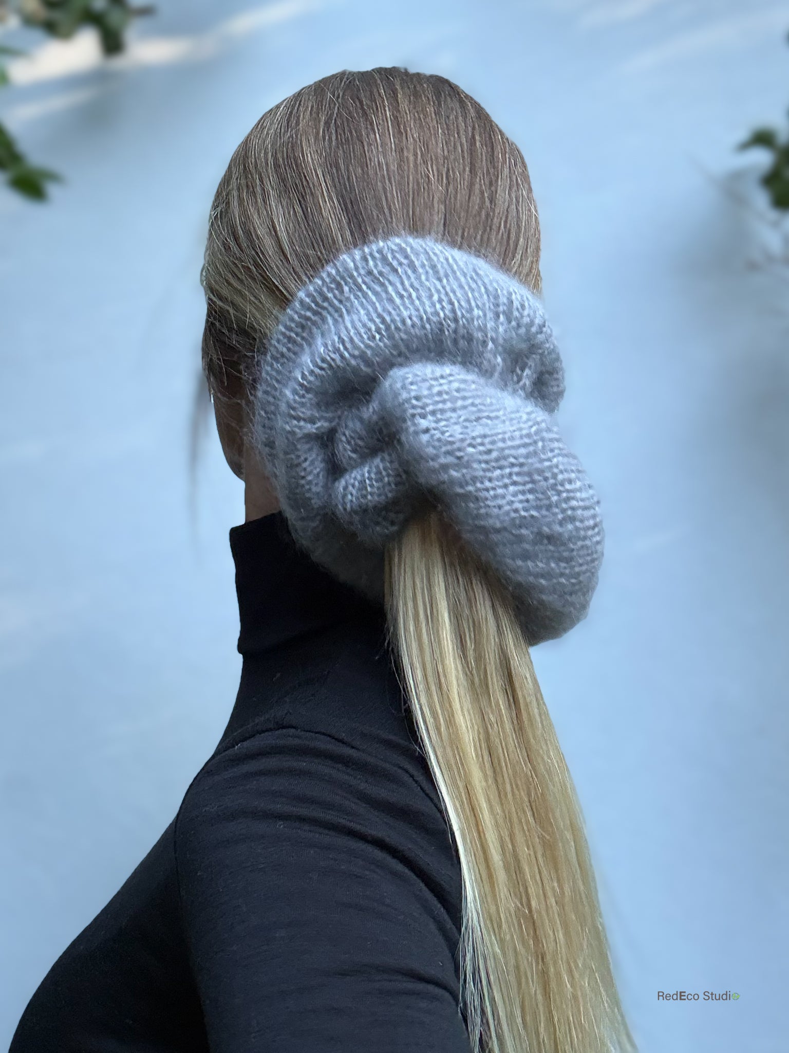 Person with a knitted gray scrunchie on their hair against a light blue background