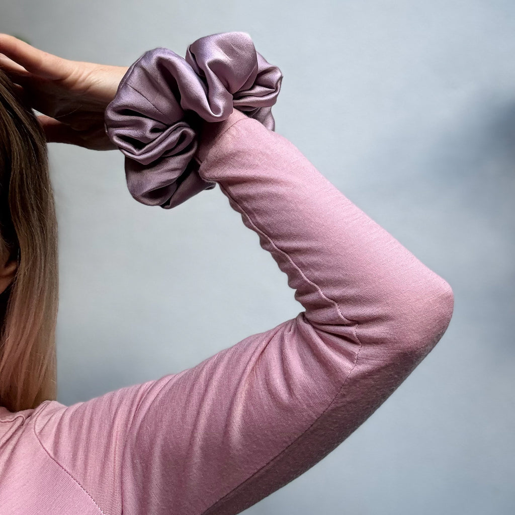 Person wearing a pink long-sleeve shirt holding a purple scrunchie against a gray background