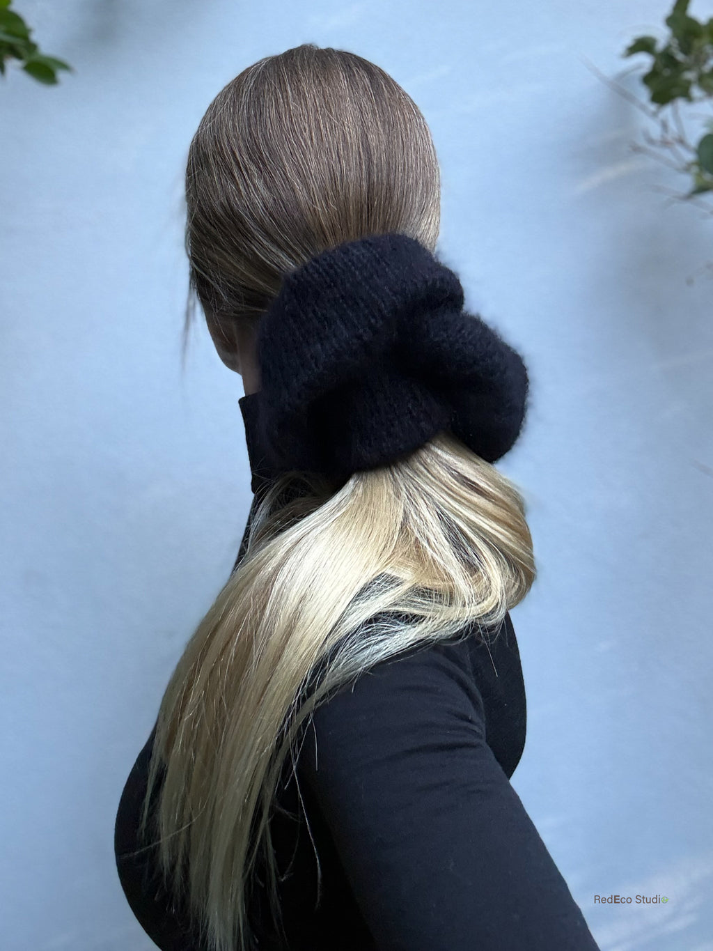 Person with long blonde hair tied in a black knitted scrunchie against a light background