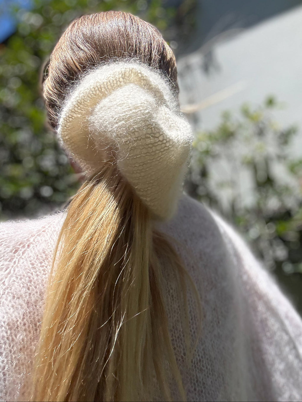 Close-up of a ponytail with a cream knitted scrunchie against a blurred natural background