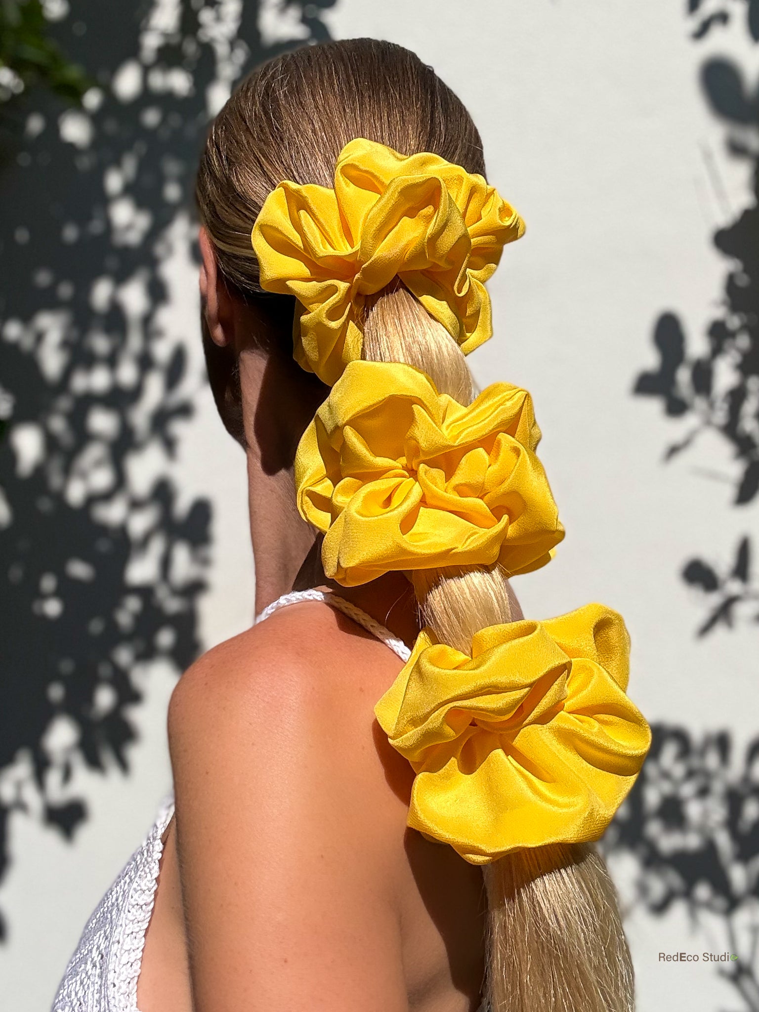 Person with a long ponytail held together with 3 yellow silk scrunchies against a light background
