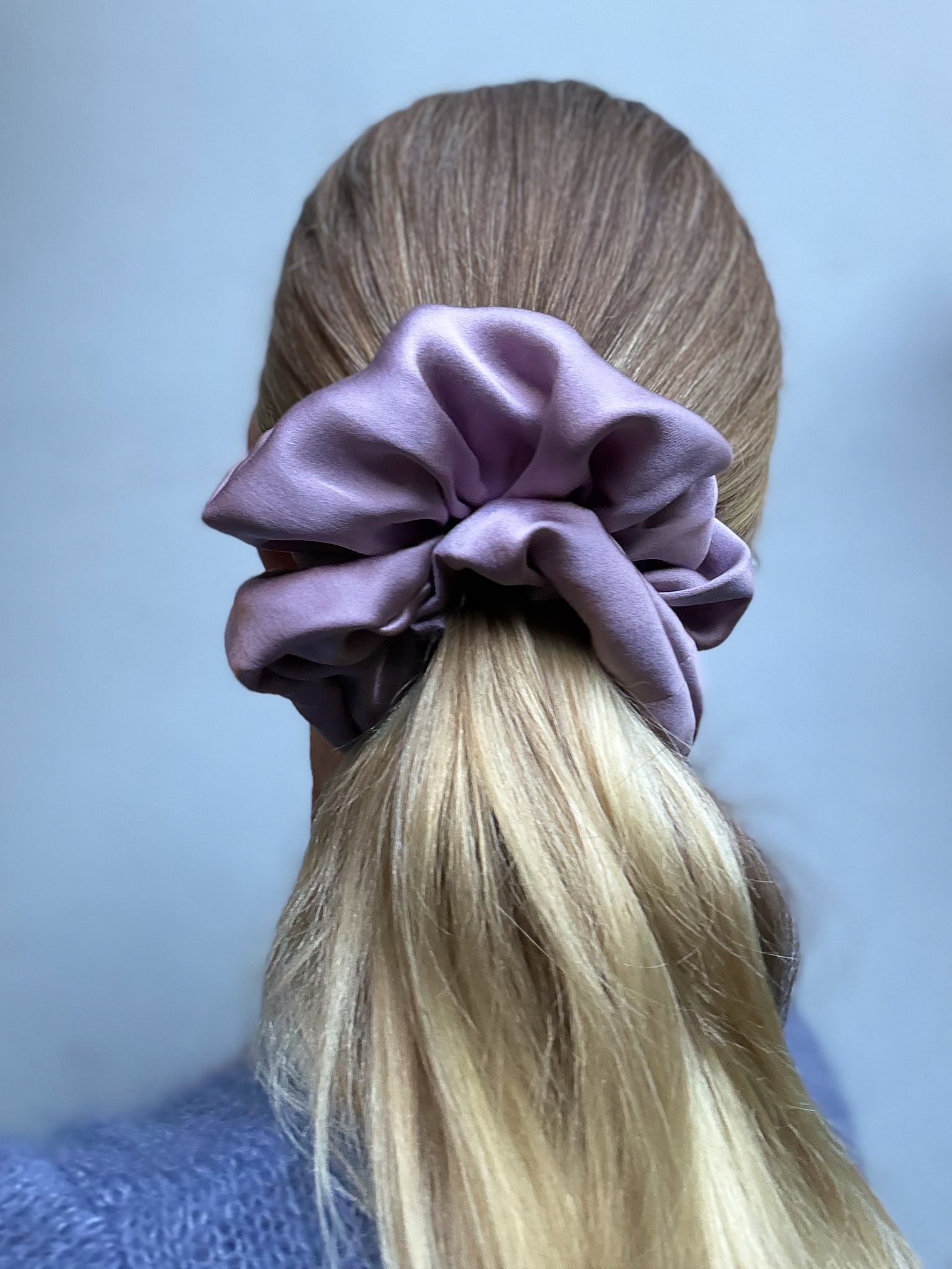 Purple scrunchie on a person's hair against a light blue background